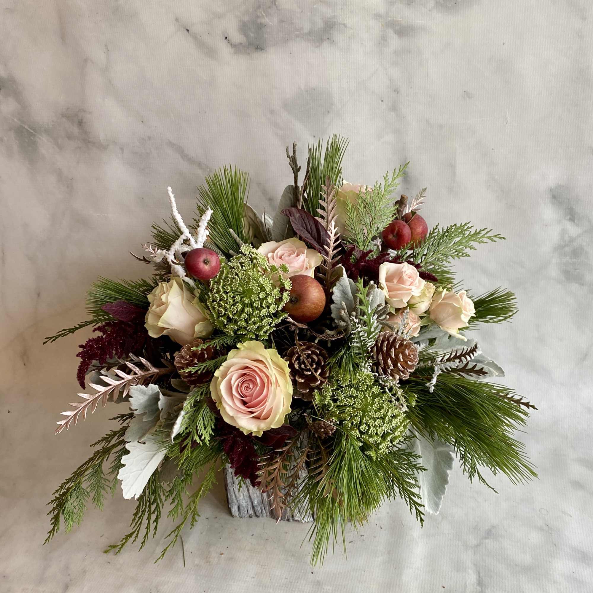 Arrangement of pale roses, pinecones, and evergreen branches in a rustic container