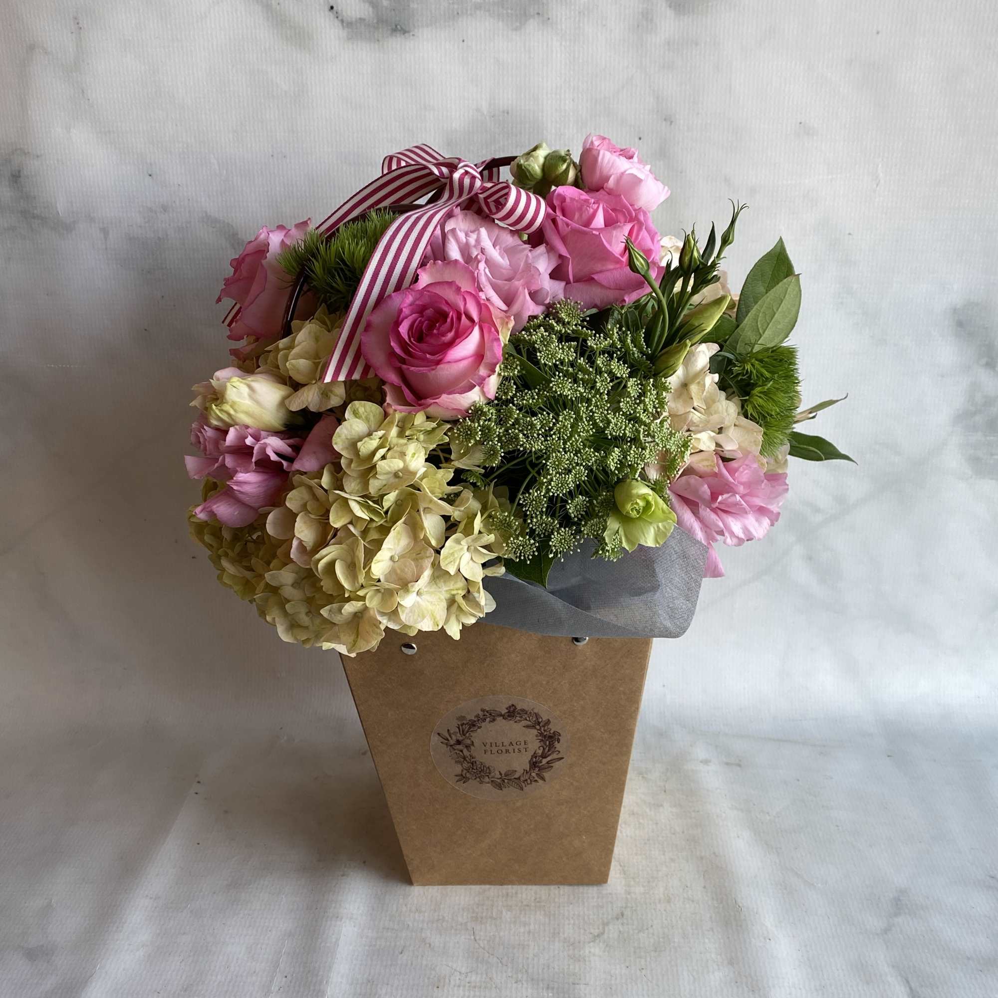 Pink roses and hydrangeas in a kraft gift box with a striped ribbon