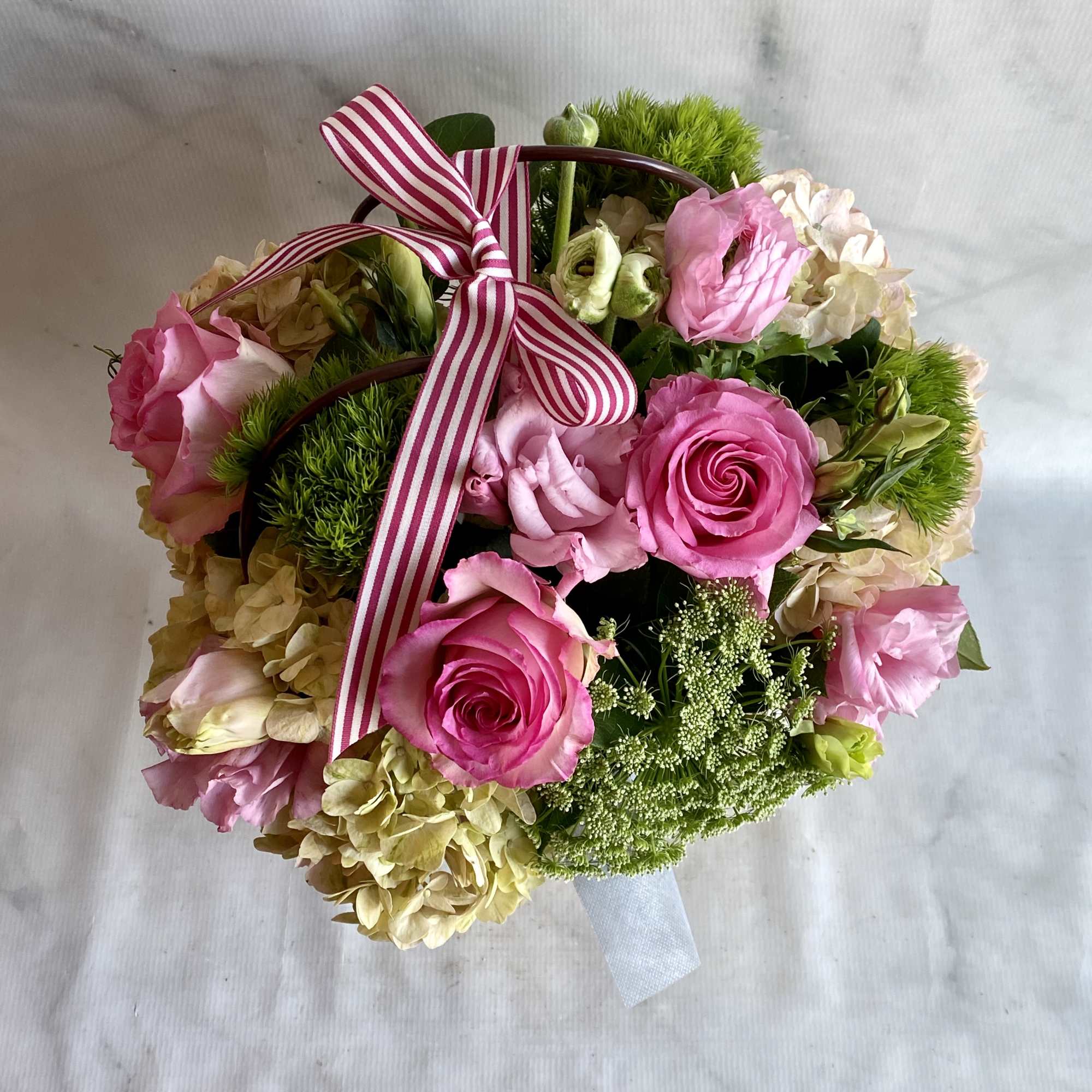 Pink roses and pale hydrangeas arranged in a basket with a striped ribbon