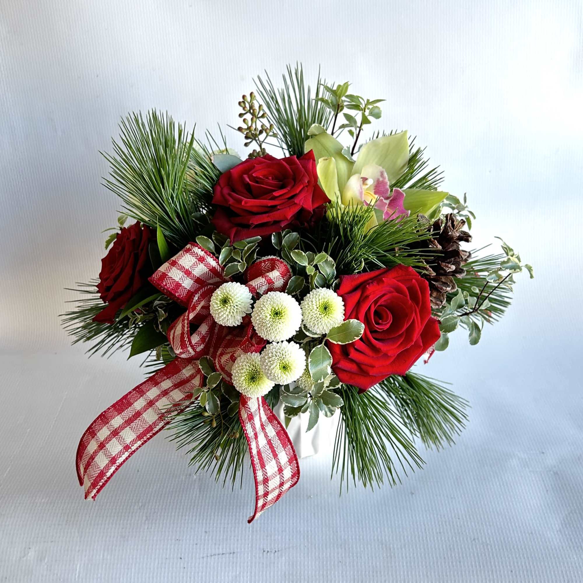 A statement piece with holiday greenery, red roses and orchids including a