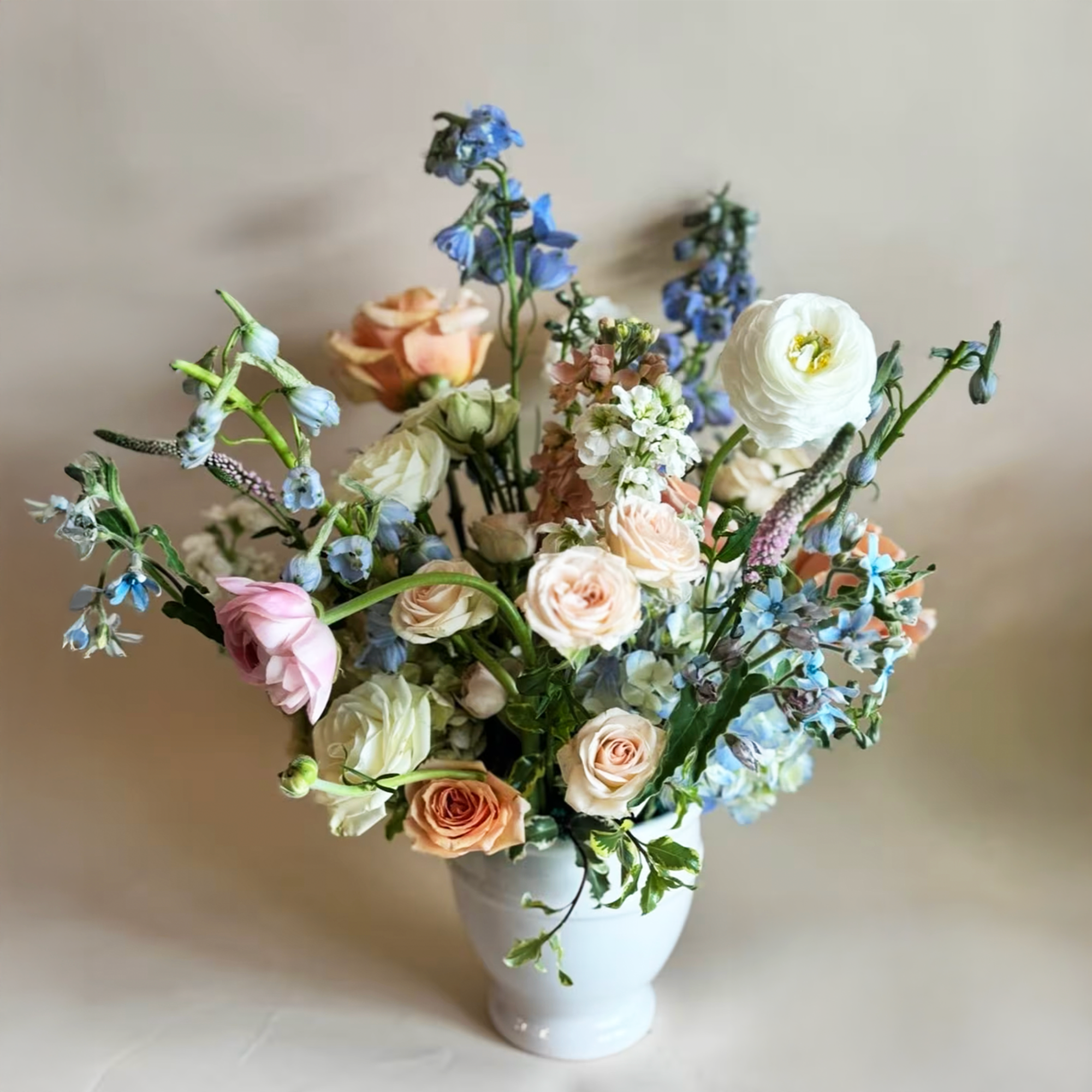 Pastel bouquet of roses, ranunculus, and blue flowers in a white vase