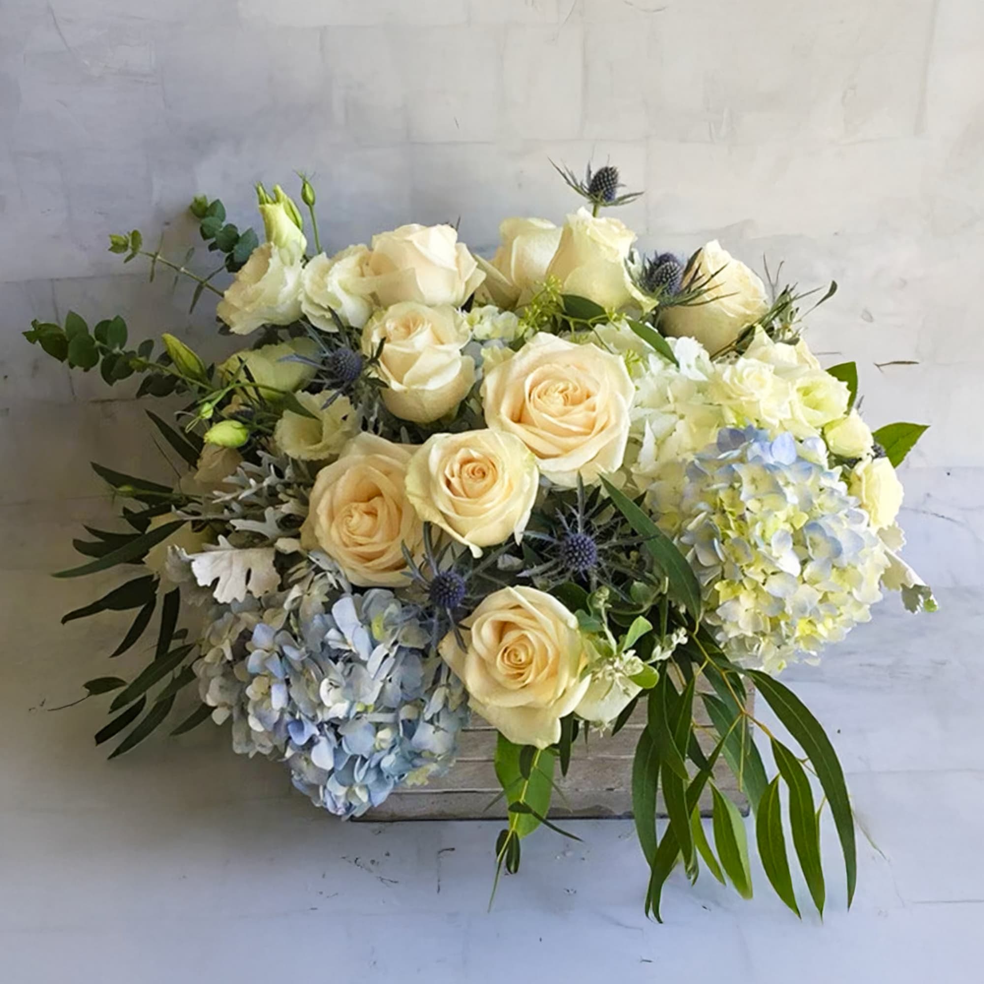 Blue hydrangeas and white roses in a wooden box.

