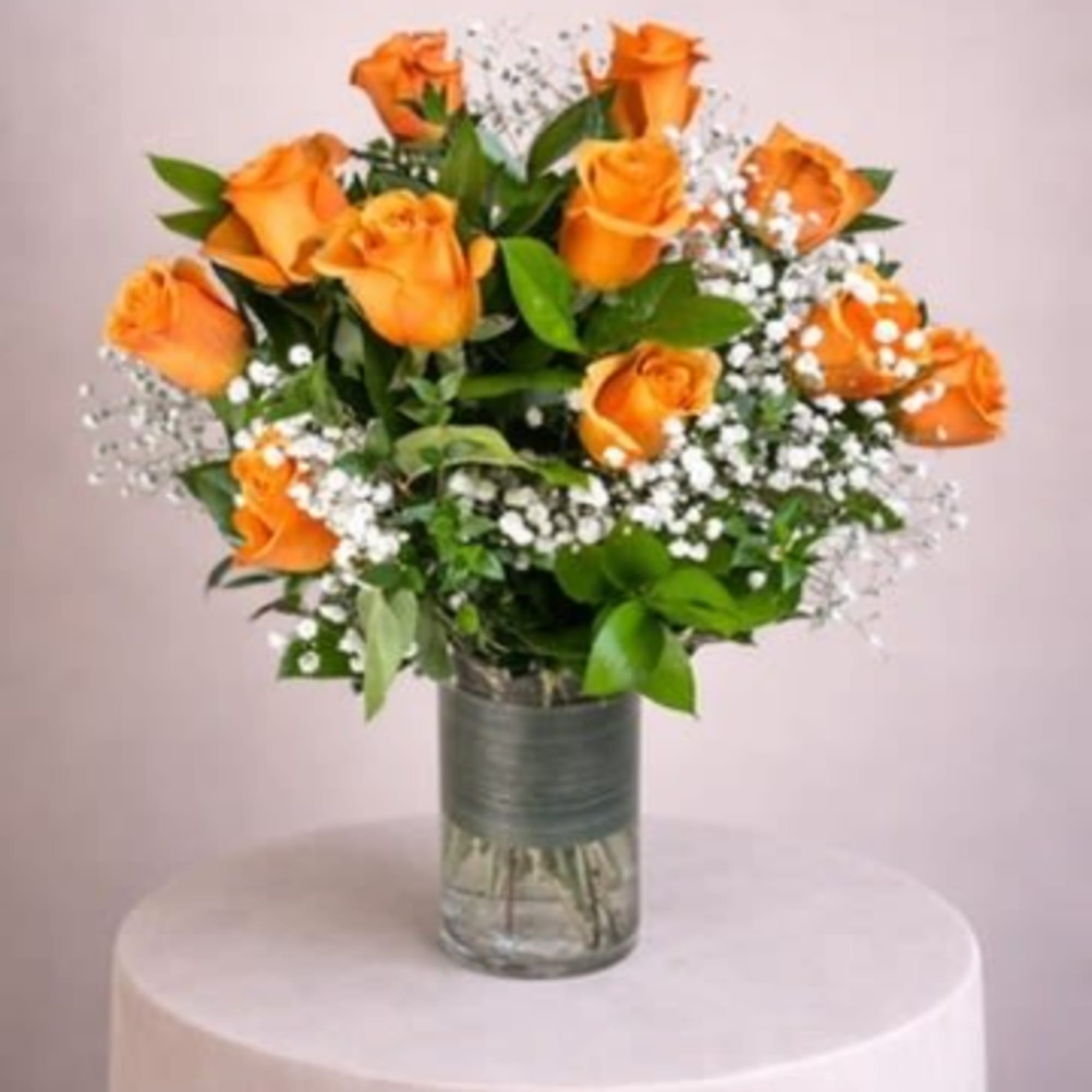 Arrangement of orange roses with white filler flowers in a clear glass cylinder vase