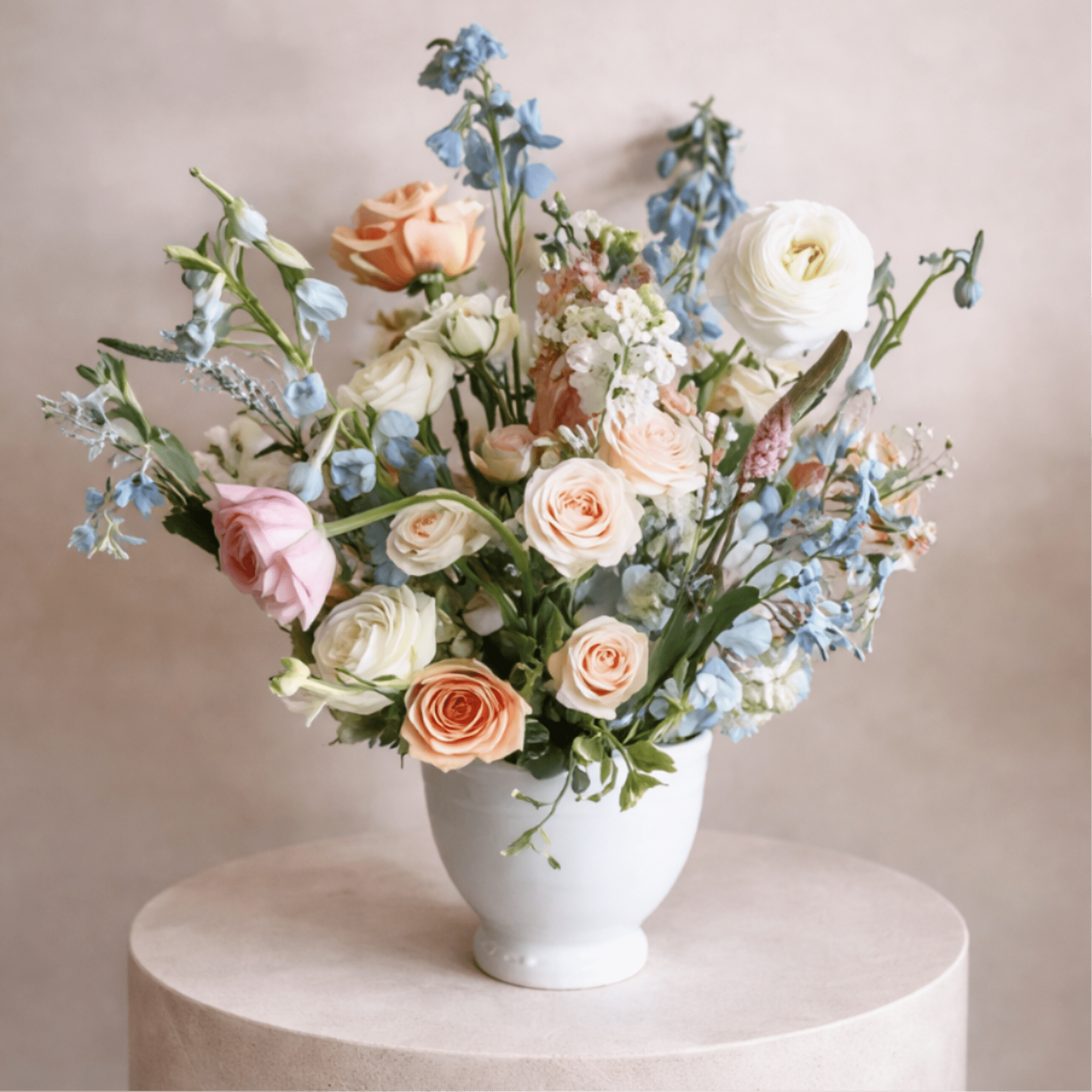 Pastel bouquet of roses and blue flowers in a white vase