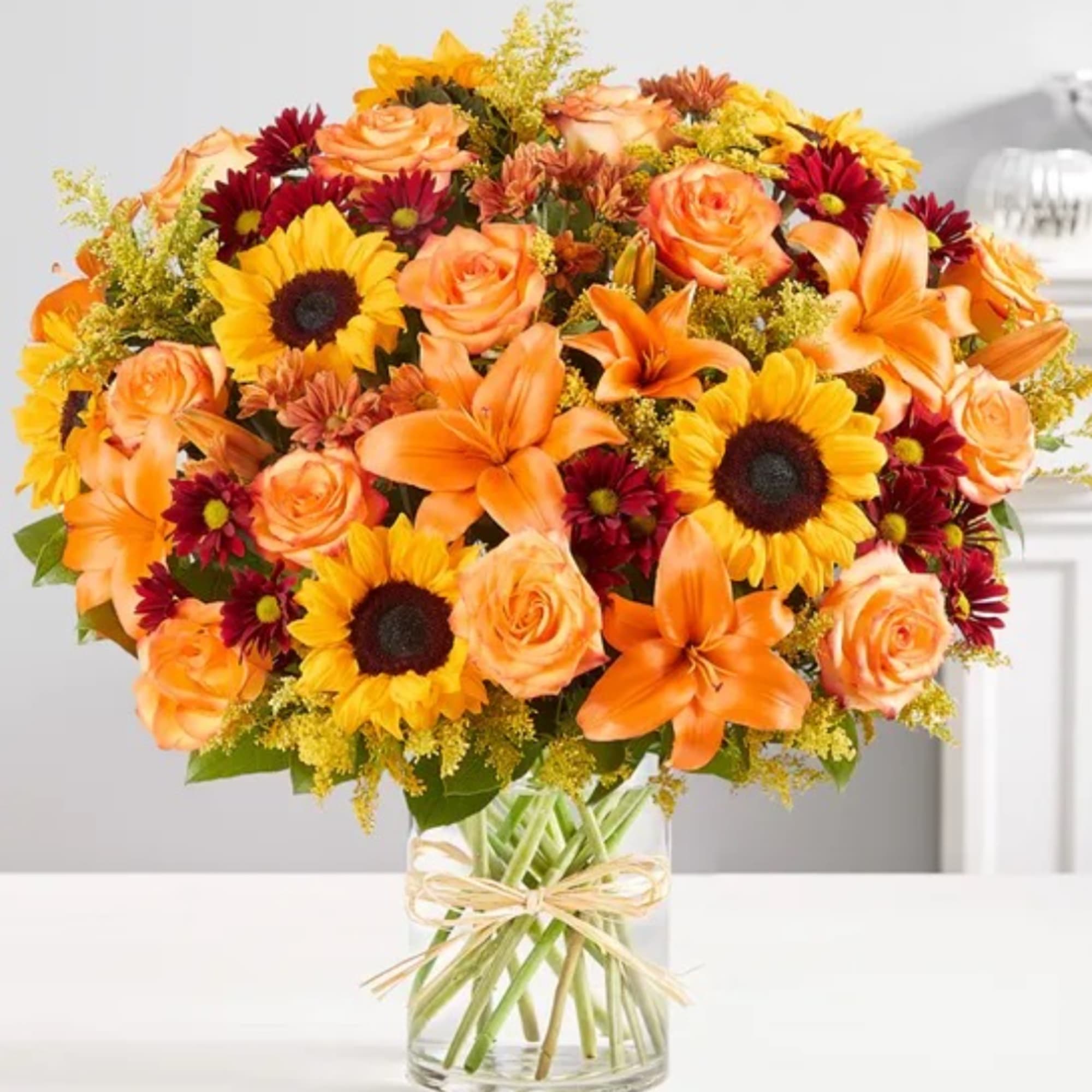 Orange and yellow mixed bouquet in a clear glass vase with a ribbon