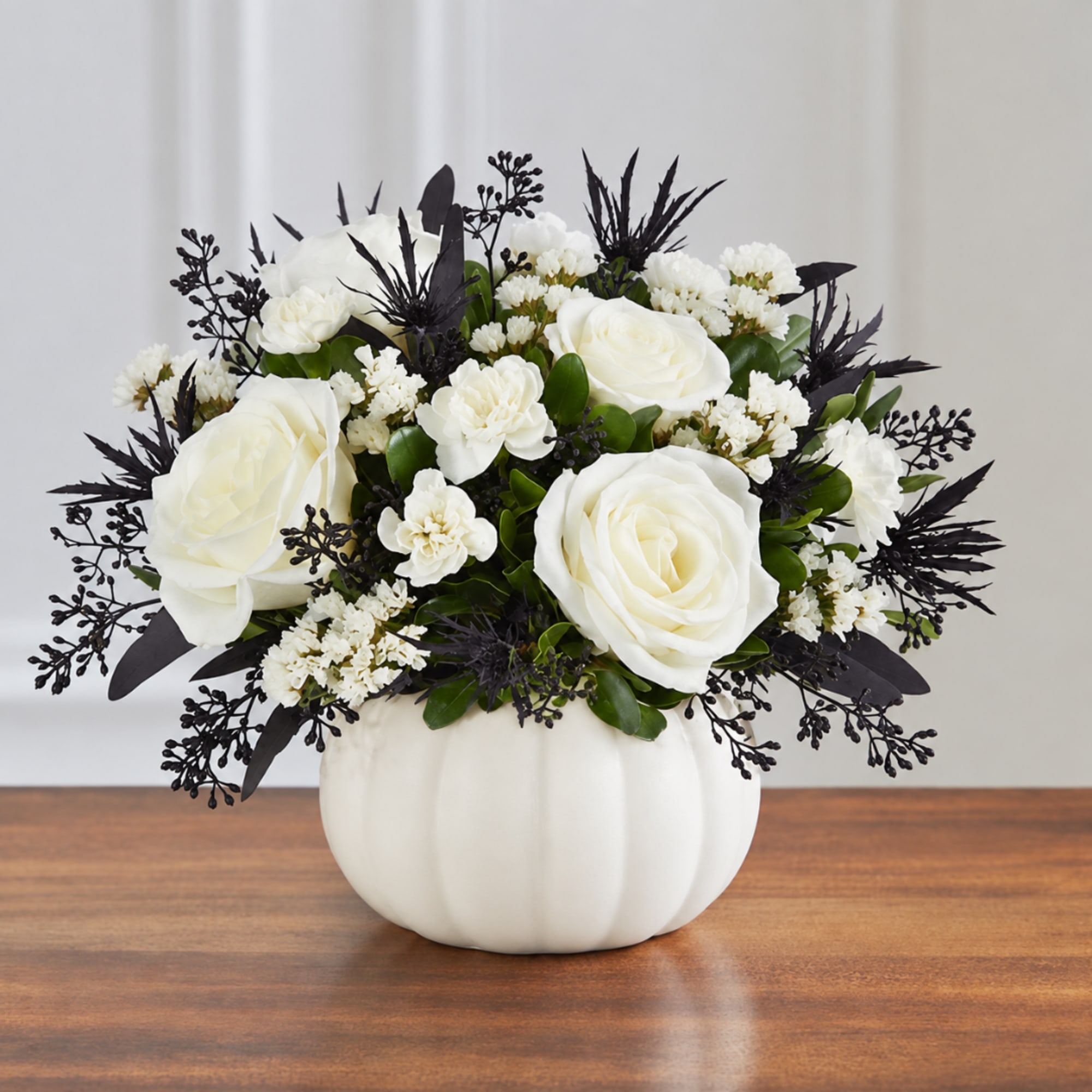White roses and small white flowers in a white pumpkin vase