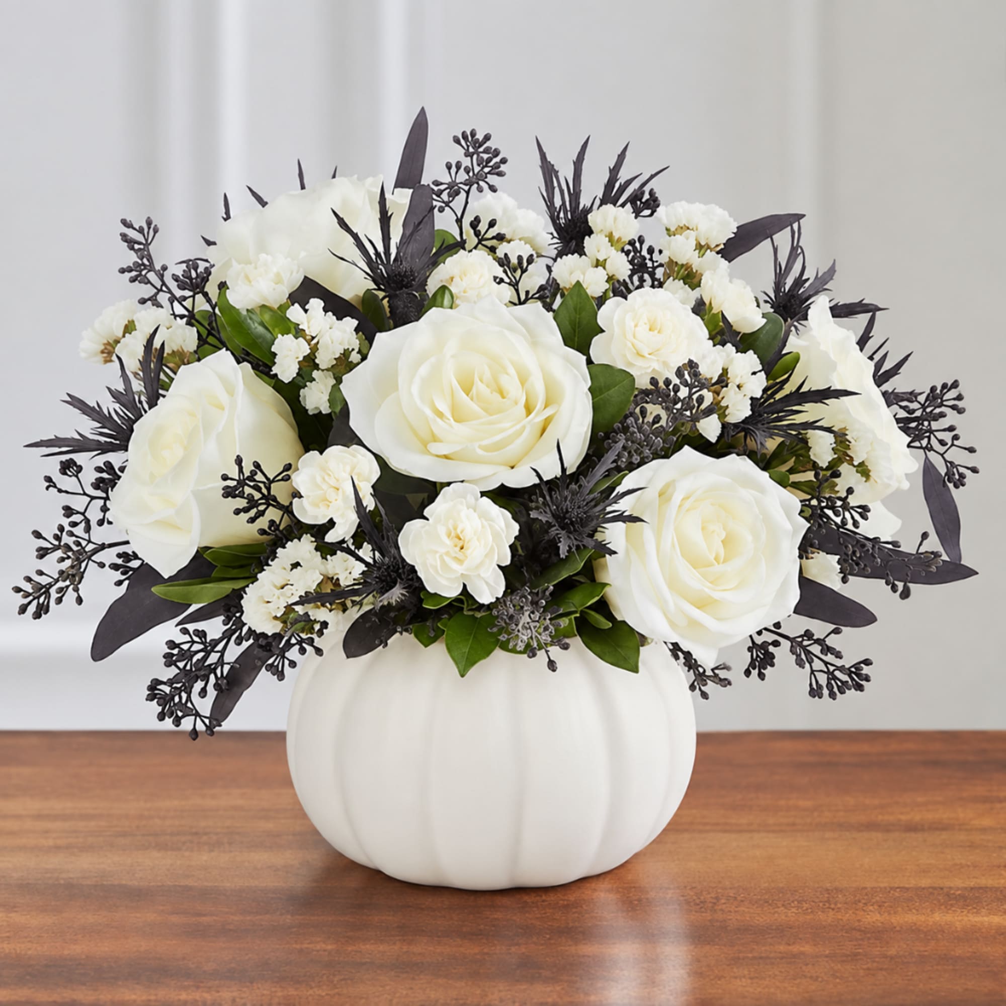 White roses and small white flowers in a white pumpkin vase