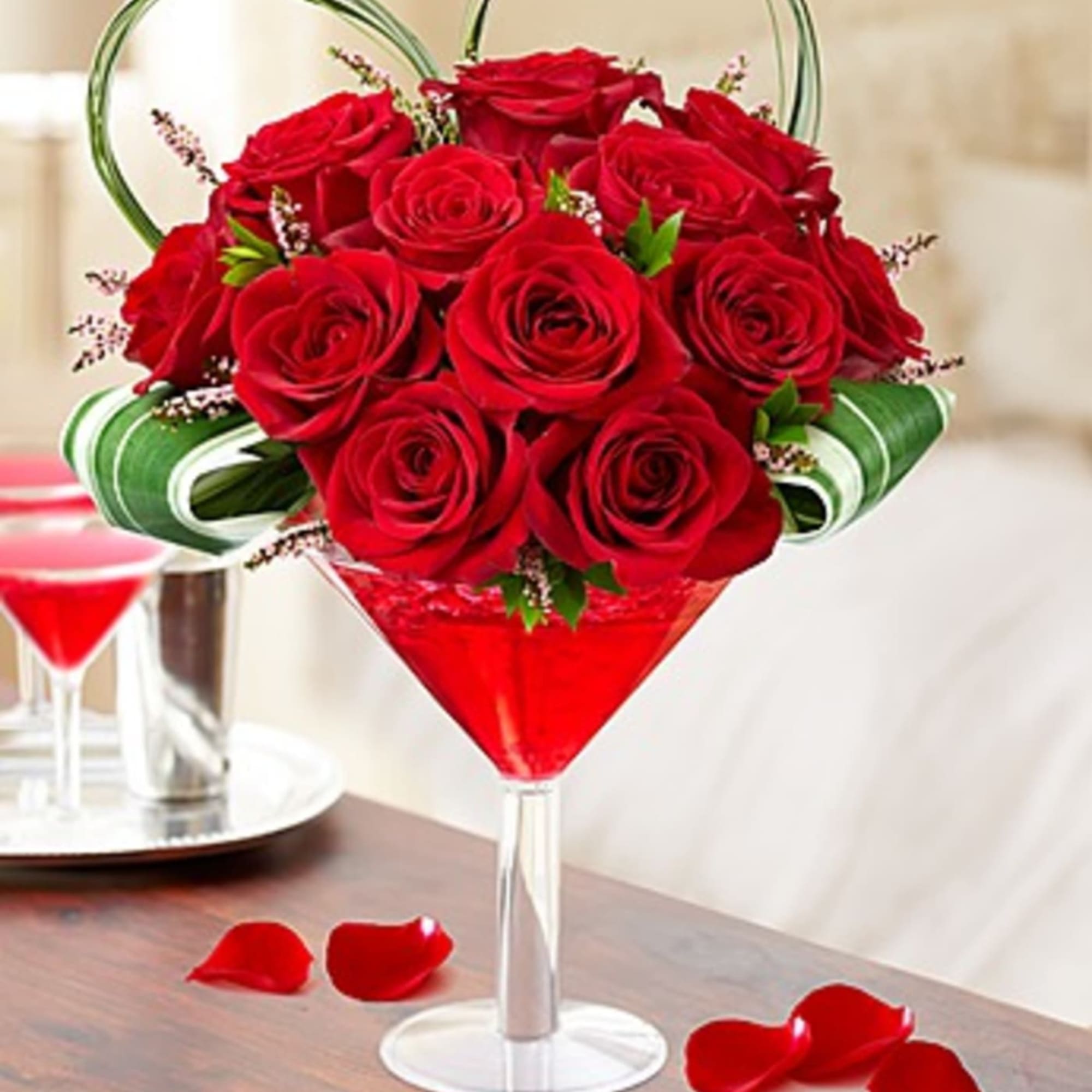 Red roses arranged in a martini glass with rose petals on the table