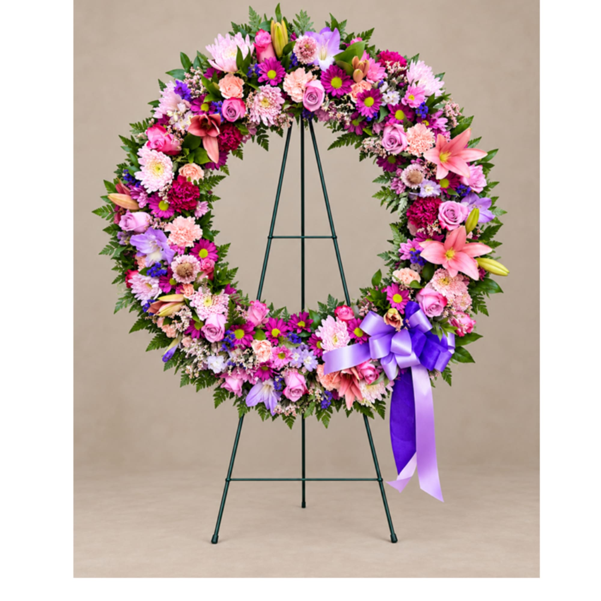 Colorful floral wreath on a stand with a purple ribbon bow