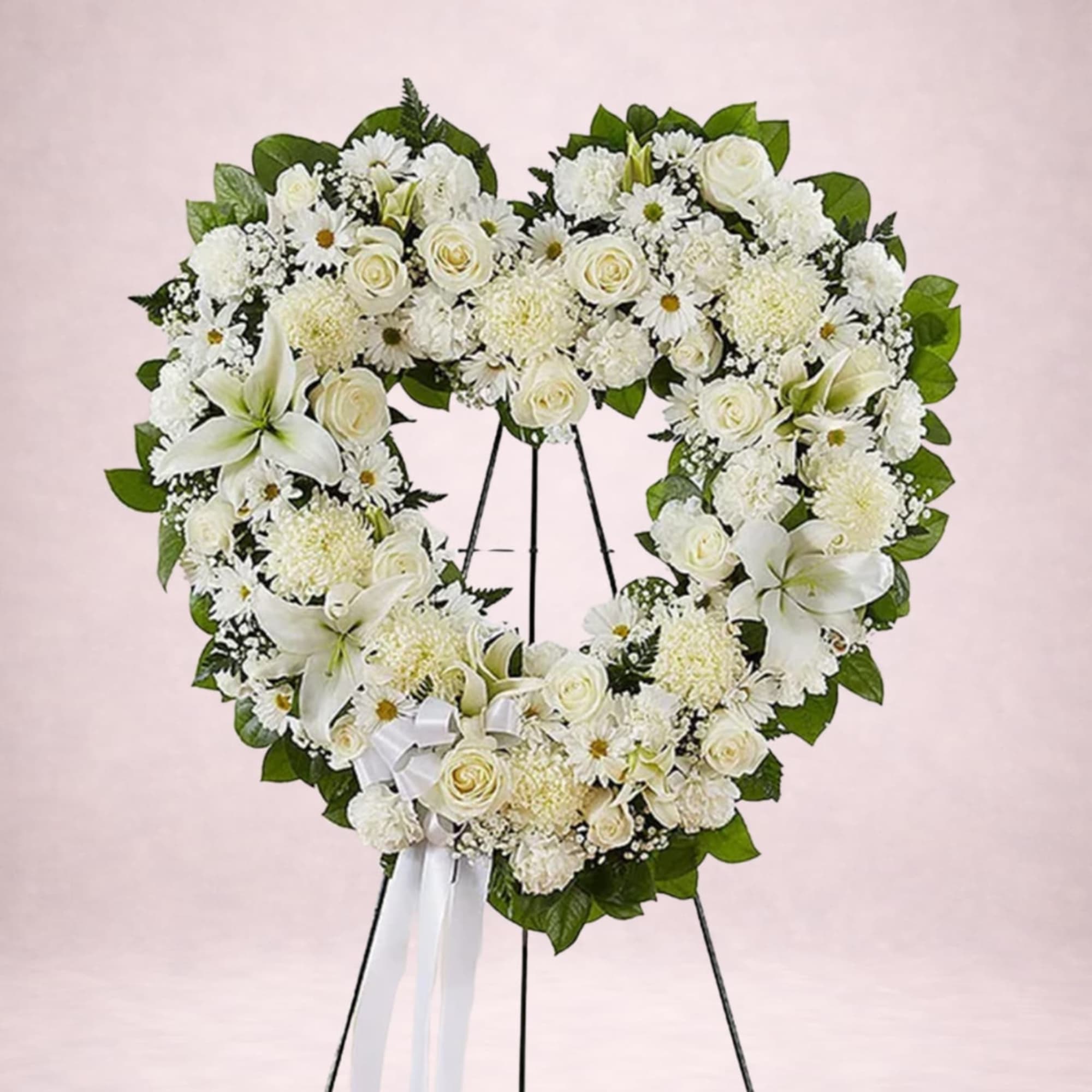 Heart-shaped white floral wreath on a stand with a white ribbon