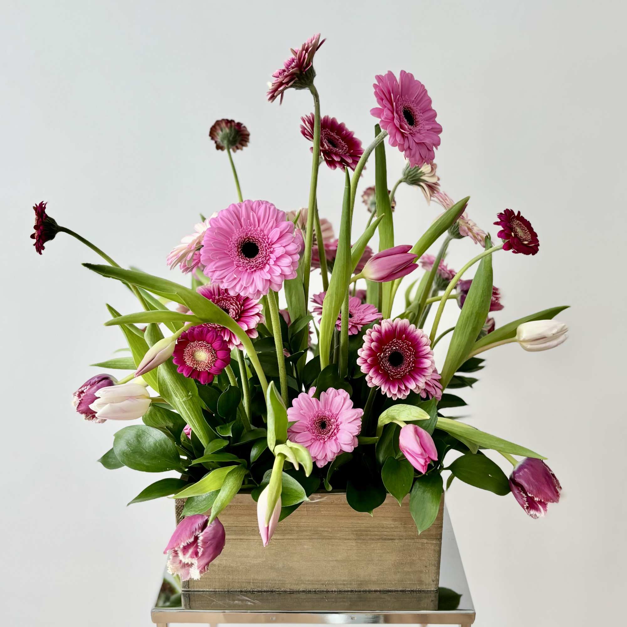 Pink gerbera daisies and tulips arranged in a wooden box