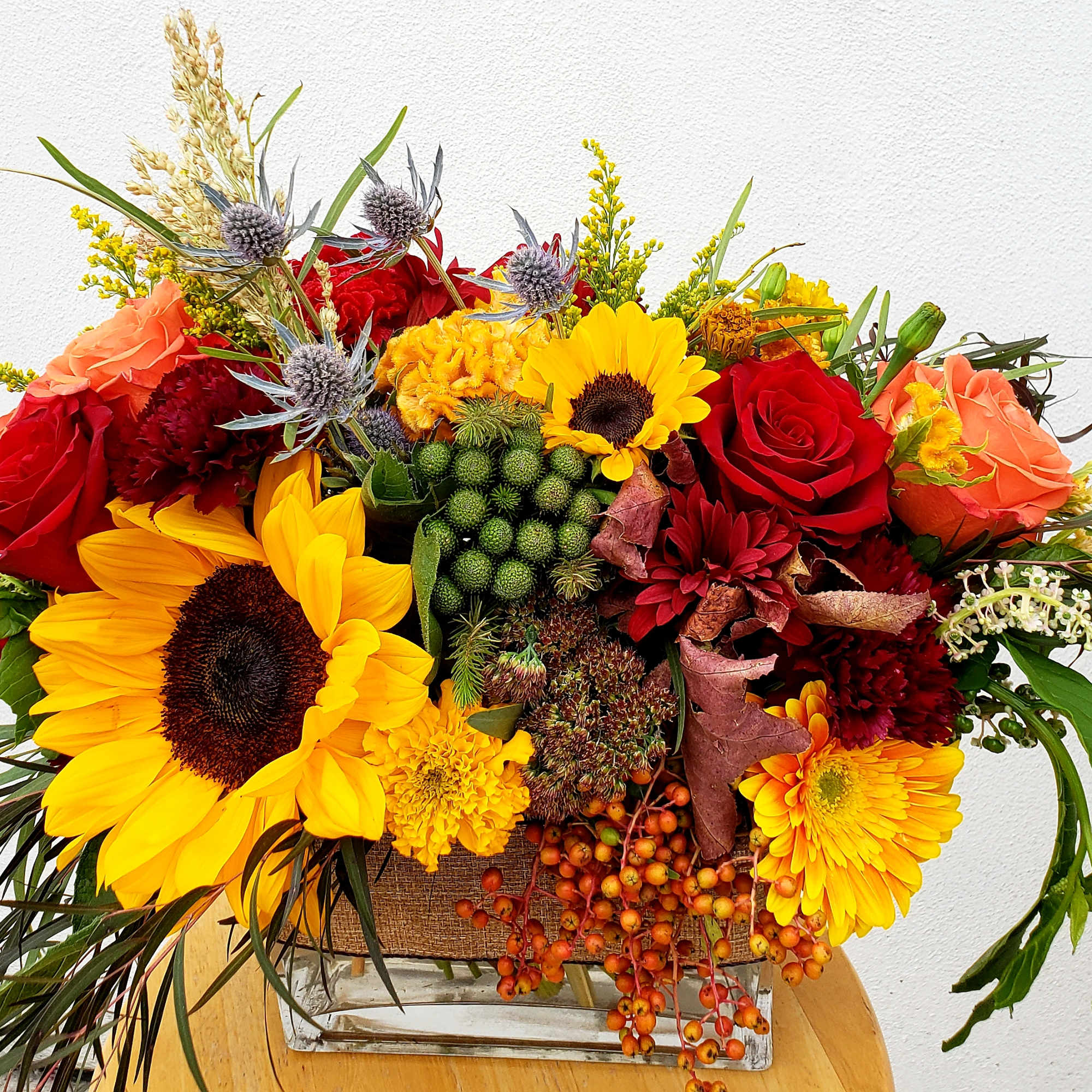 Bright mixed bouquet with sunflowers, roses, and orange blooms in a glass vase