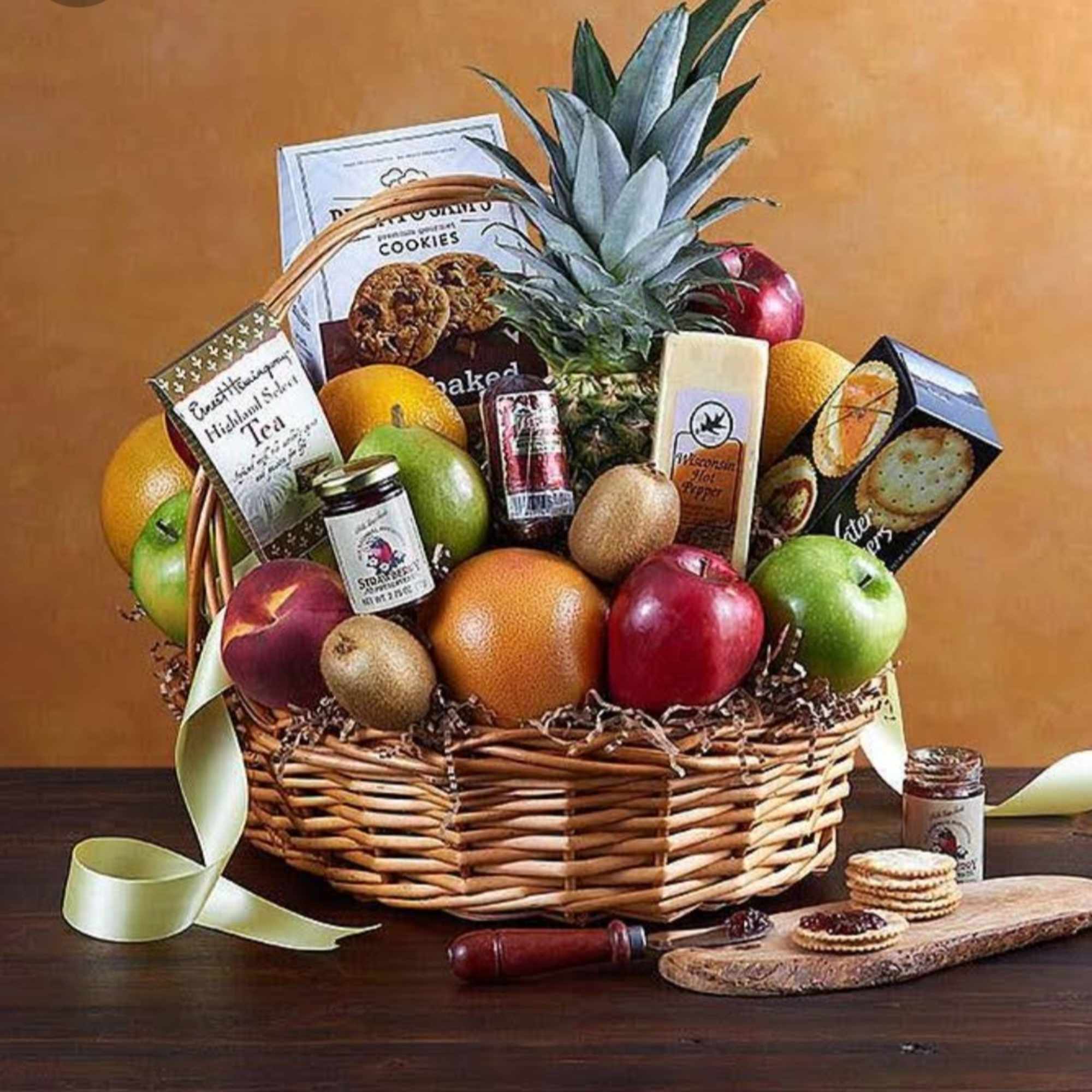 Fruit and snack gift basket with a pineapple, apples, oranges, tea, cookies, and jam