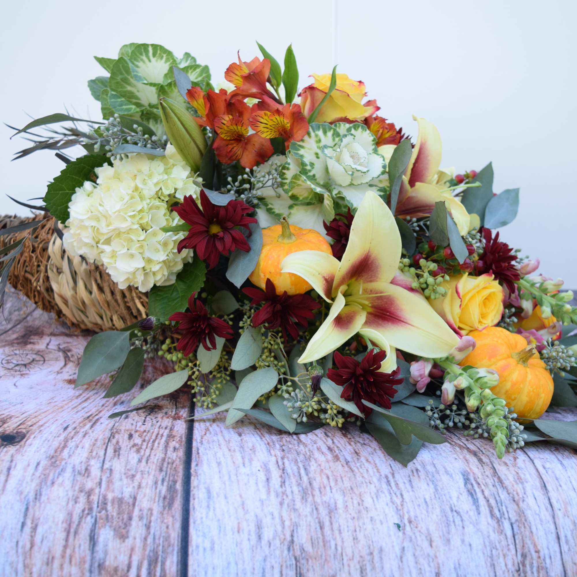 Mixed autumn bouquet with lilies, roses, hydrangea, and small pumpkins in a wicker basket