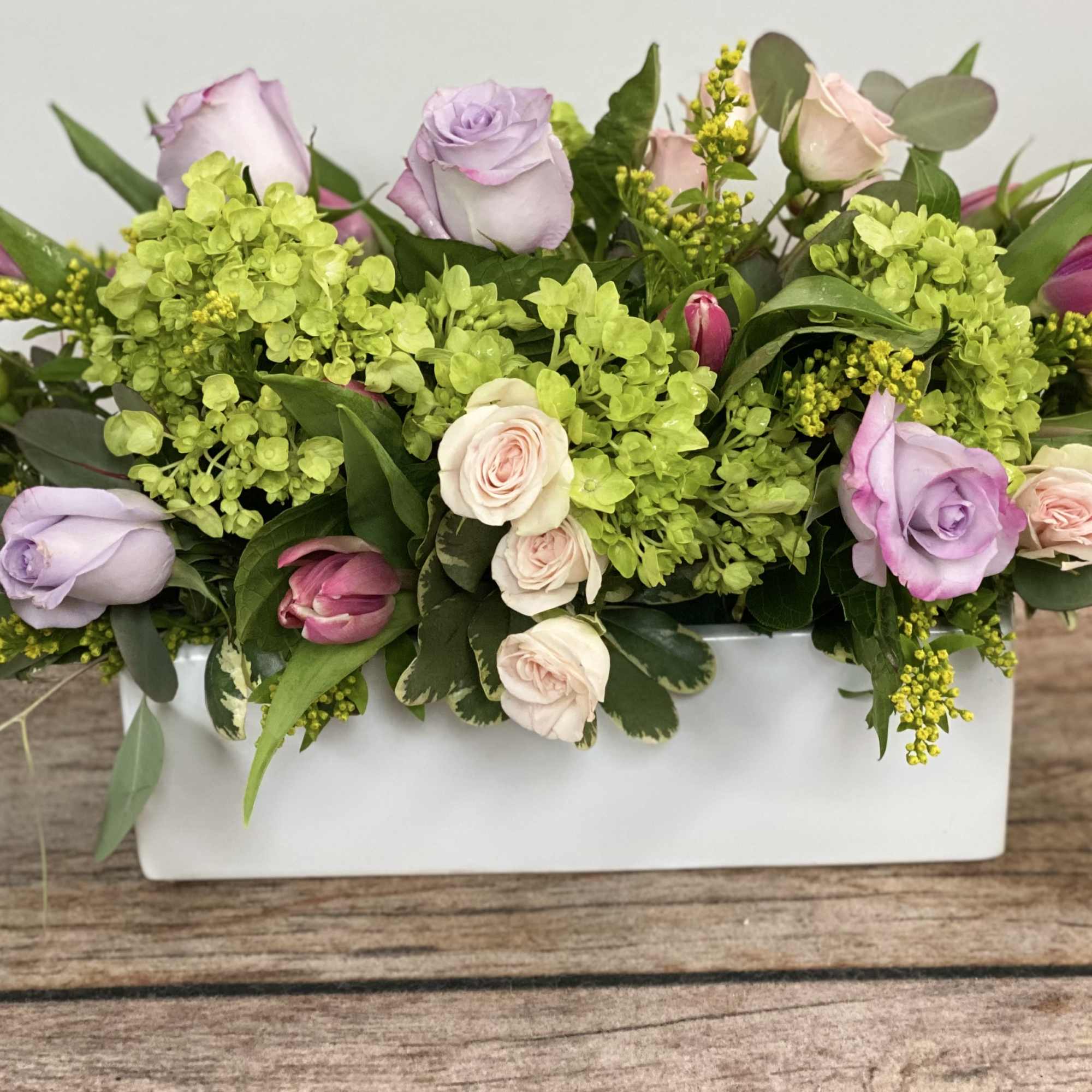 Rectangular floral arrangement with pastel roses and green hydrangeas in a white vase