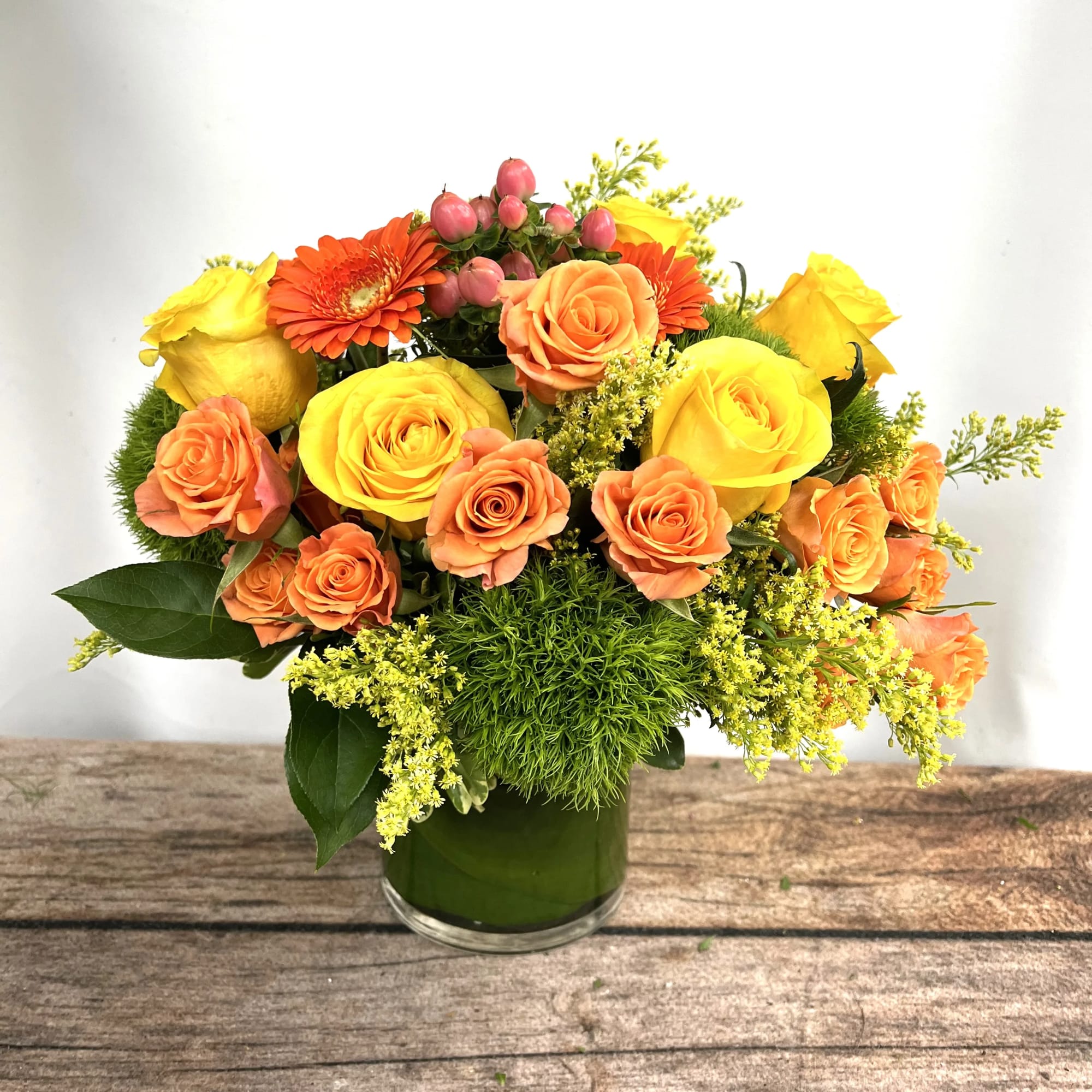 Bouquet of yellow and orange roses with orange gerbera daisies in a glass vase