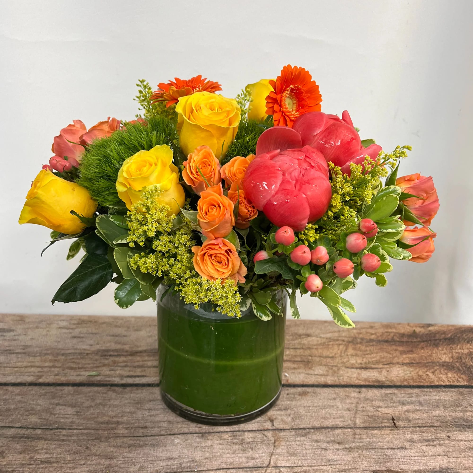 Mixed bouquet of yellow, orange, and pink flowers in a green glass vase