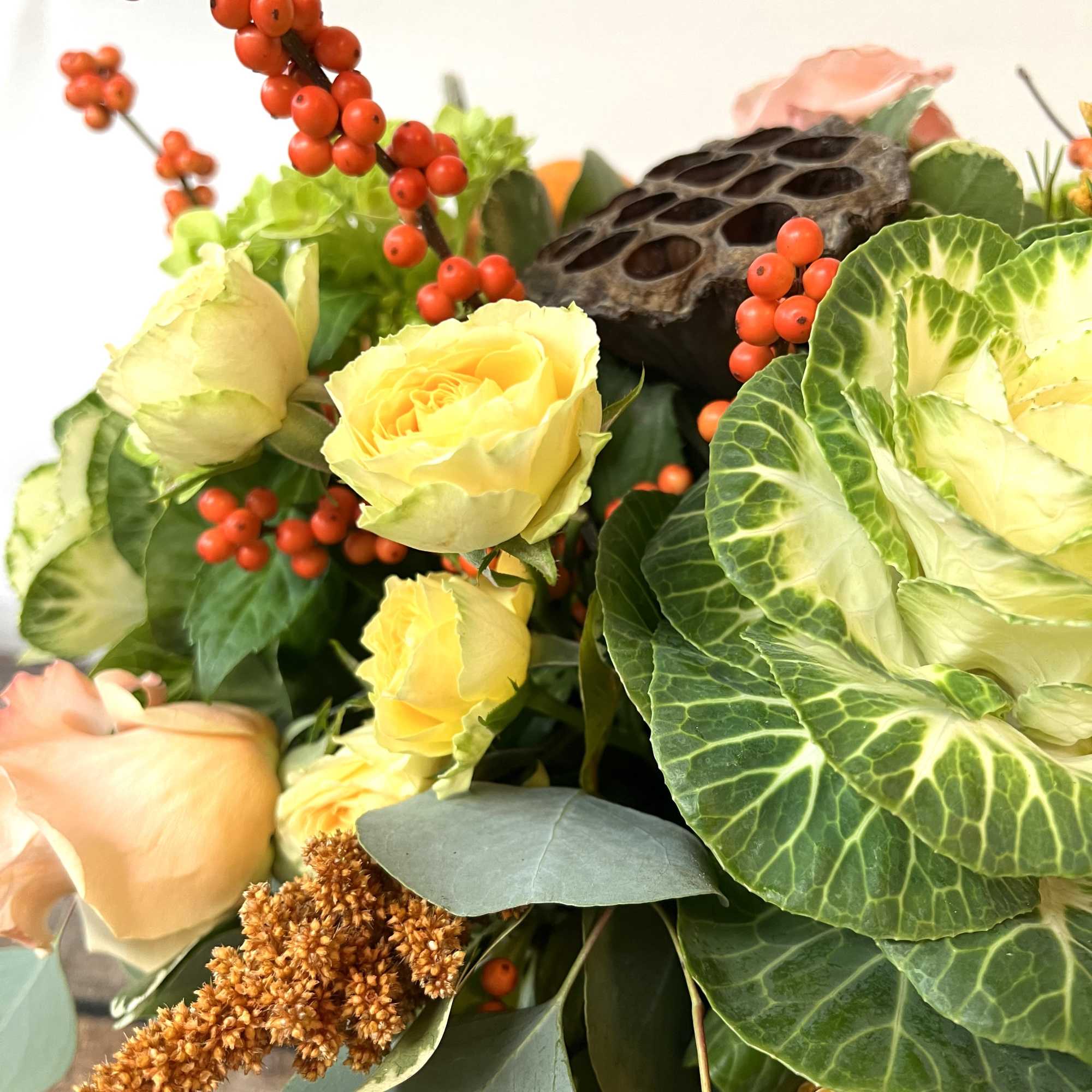 Bouquet of pale yellow roses with red berries and large green leaves