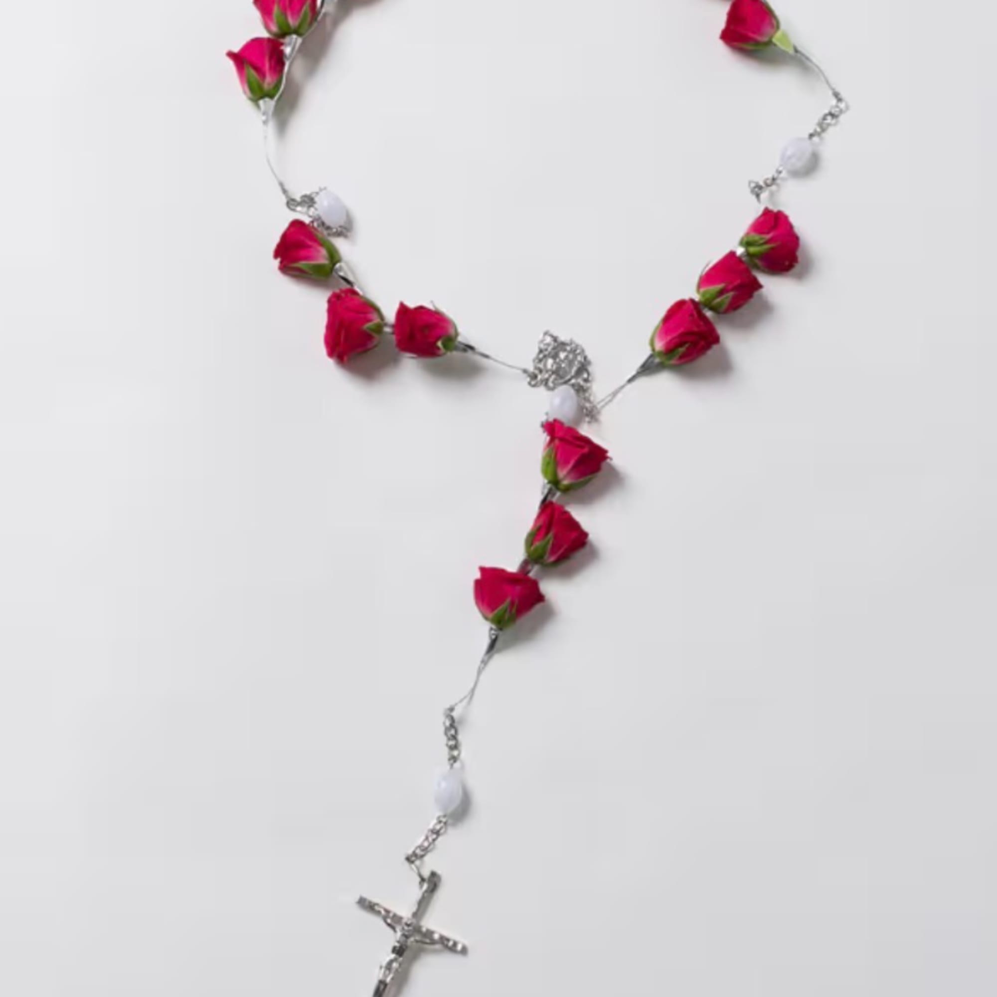 Pink rosebud rosary laid on a white background