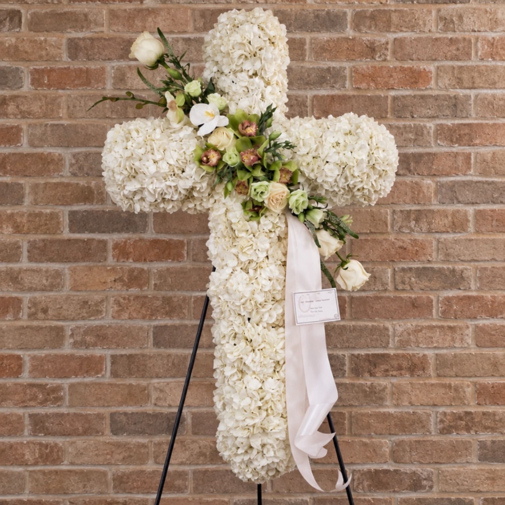 White floral cross arrangement with roses and ribbon on a stand
