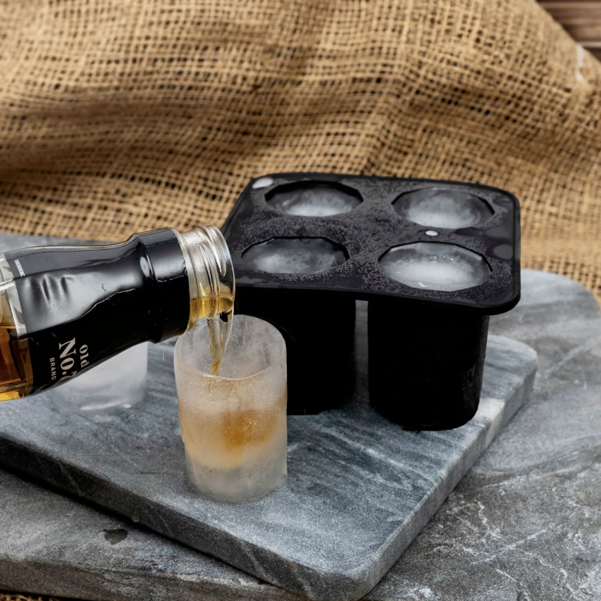 Bottle pouring liquor into a frosted shot glass beside an ice mold