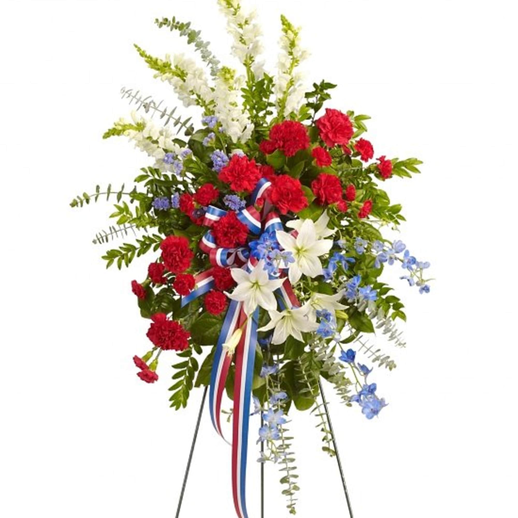 Standing floral spray with red carnations, white lilies, and blue accents on an easel