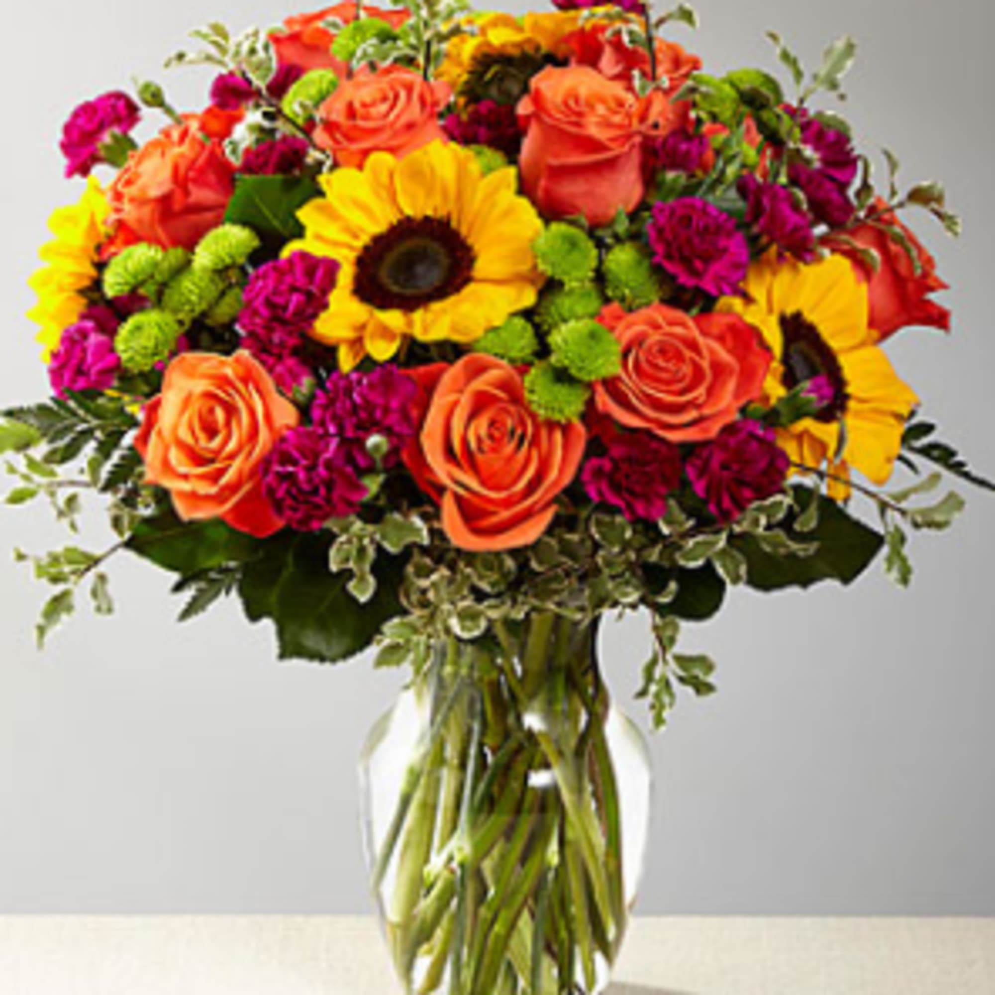 Bouquet of orange roses, sunflowers, and magenta flowers in a glass vase