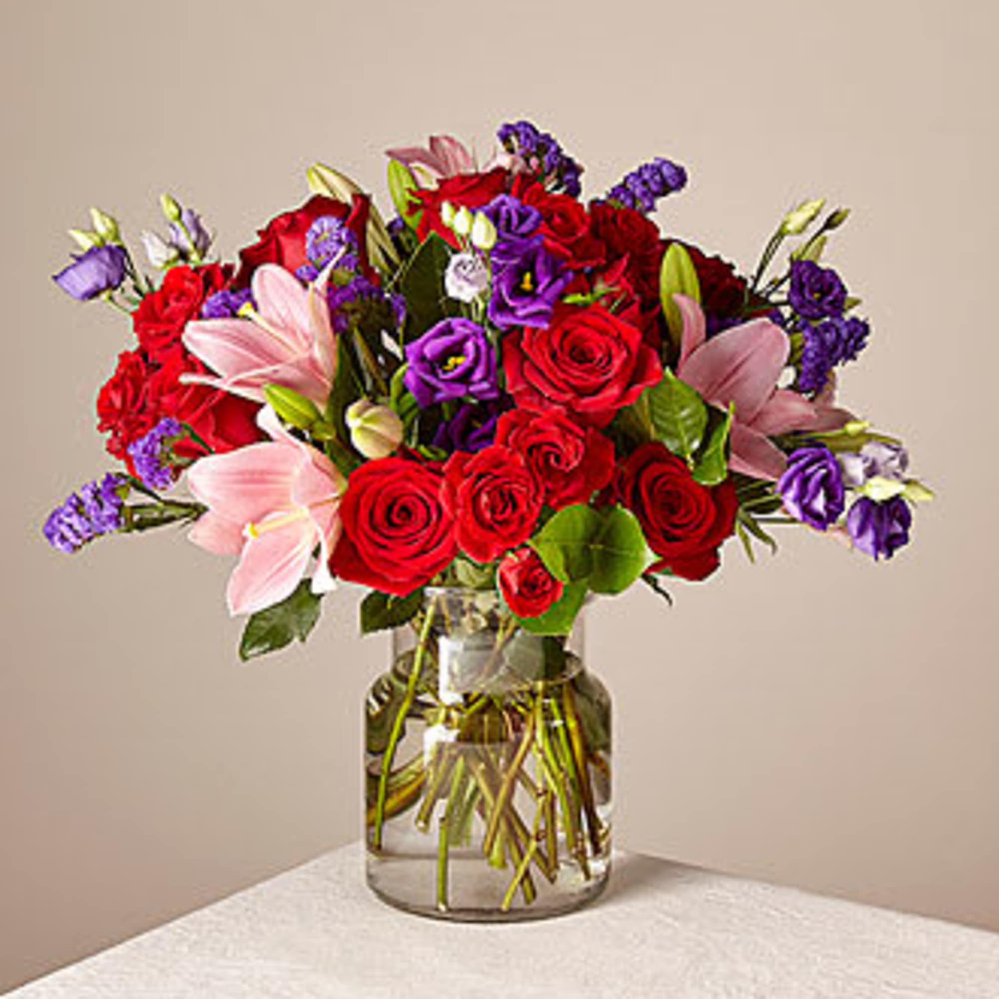 Bouquet of red roses, pink lilies, and purple flowers in a glass vase