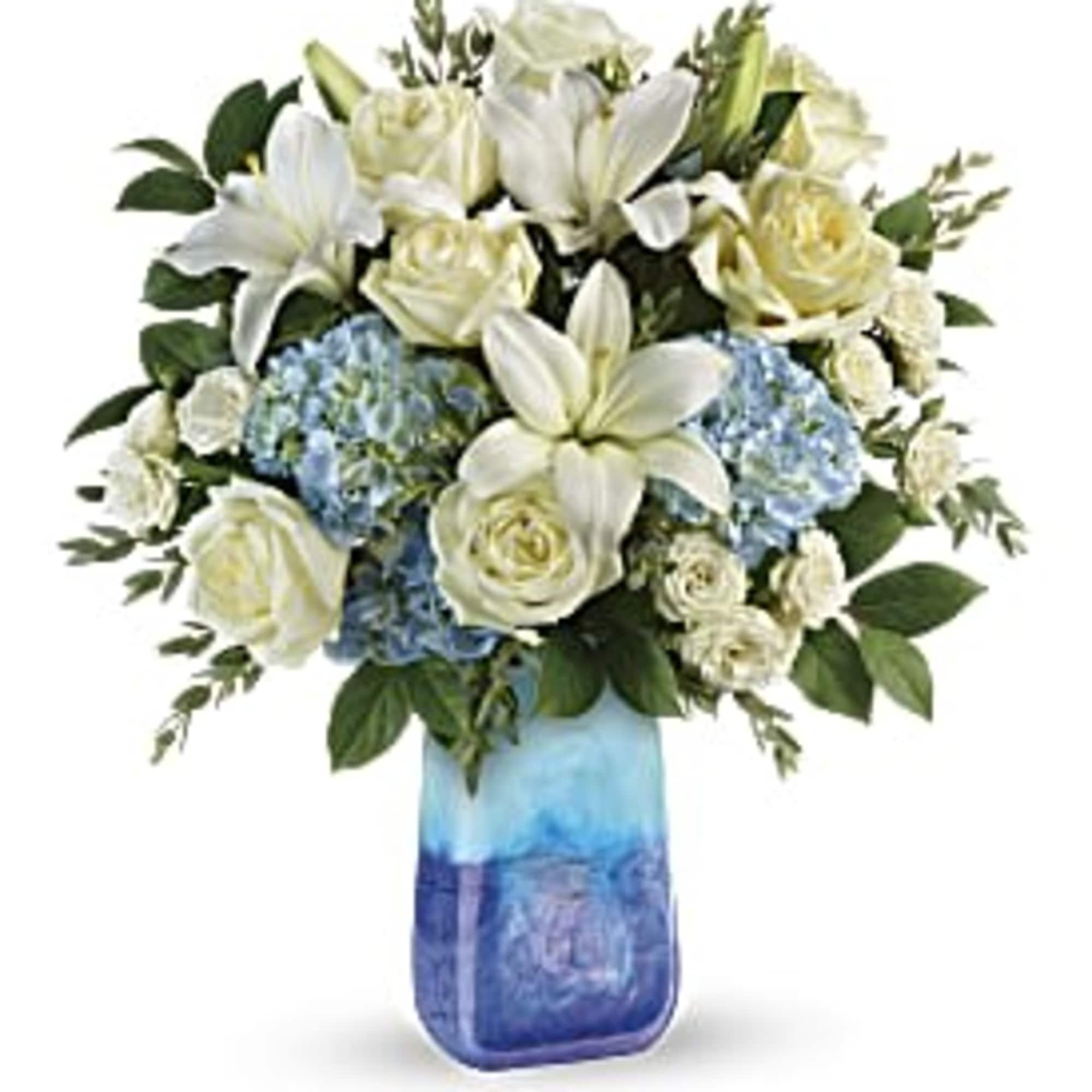 White lilies and roses arranged with blue hydrangeas in a blue glass vase