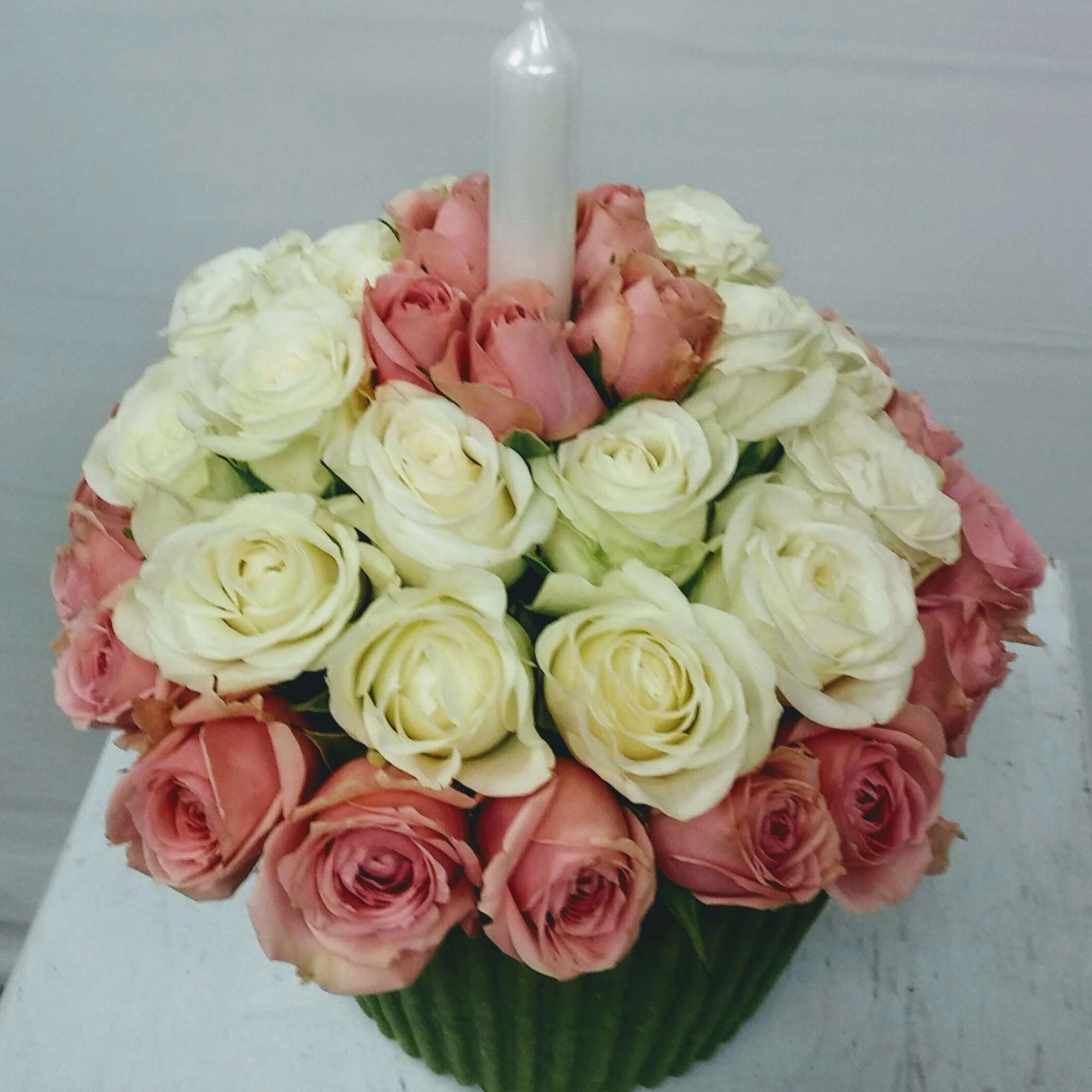 Pink and white roses arranged around a tall white candle in a round container
