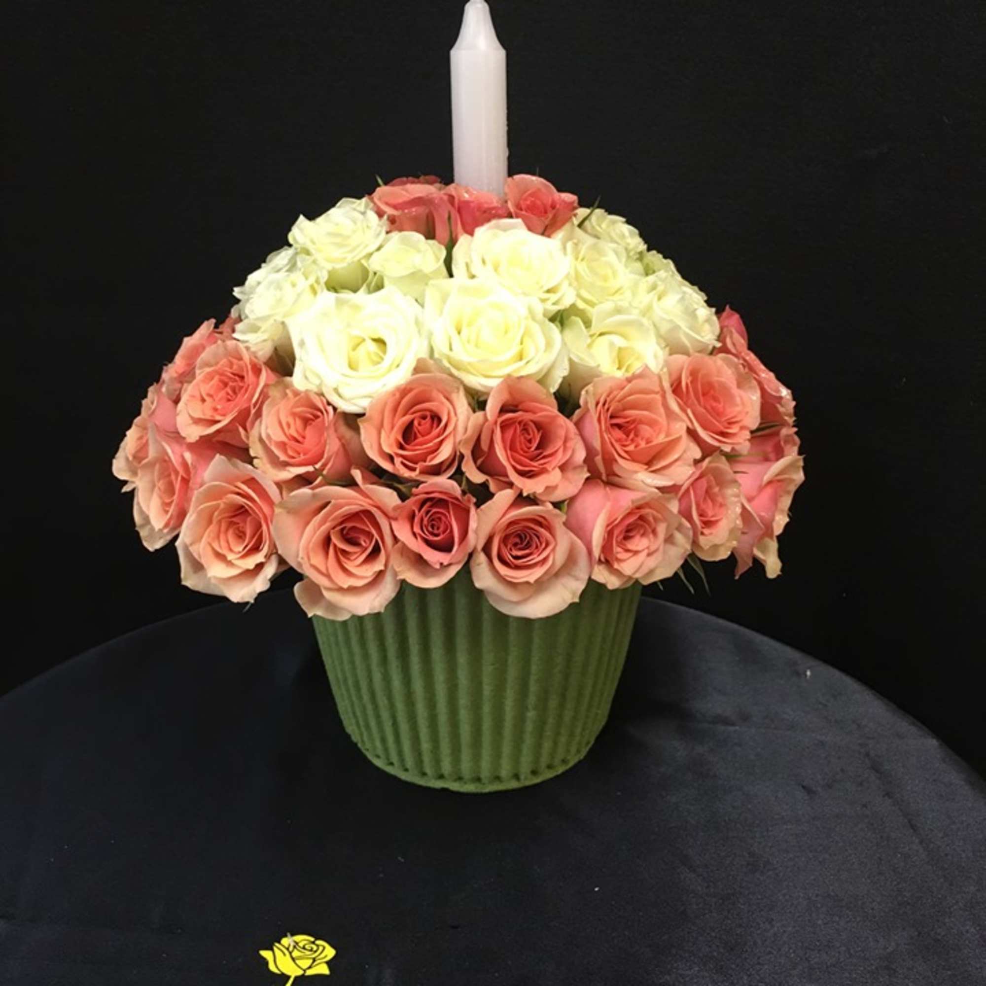 Pink and white rose arrangement in a green vase with a white candle