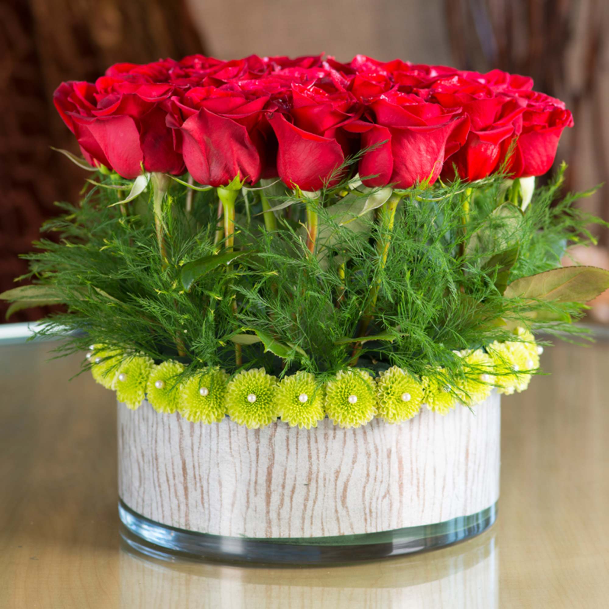 Red roses arranged in a low glass vase with green accents