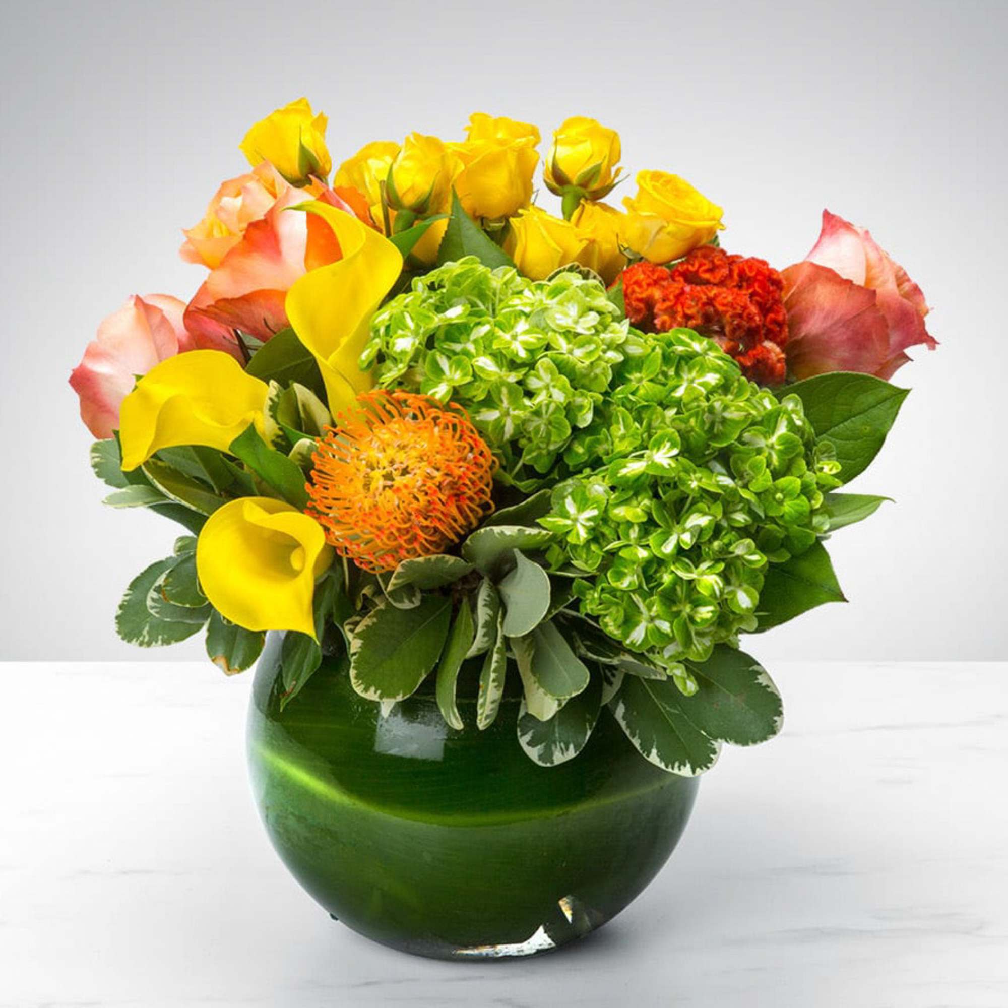 Bouquet of yellow roses, calla lilies, and green hydrangeas in a green glass vase