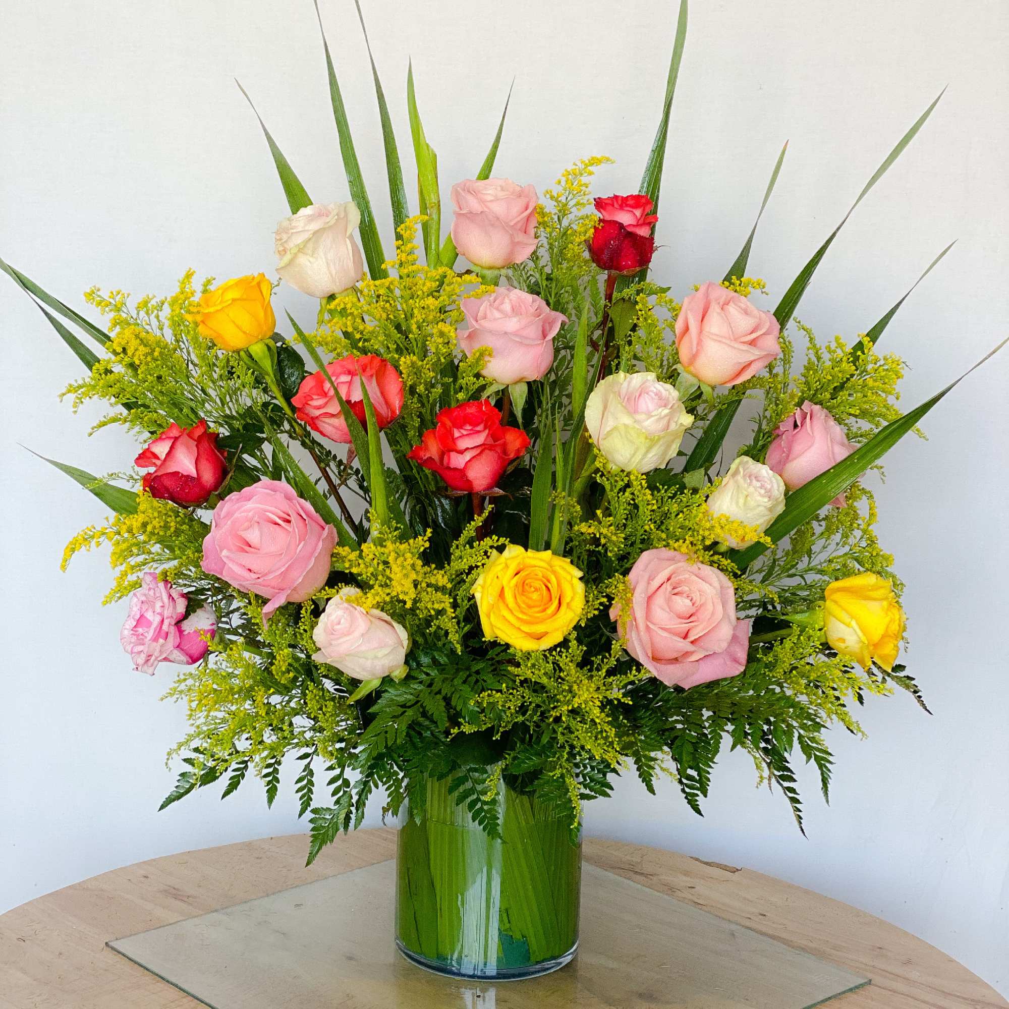 Mixed roses in pink, yellow, and red arranged in a clear glass vase