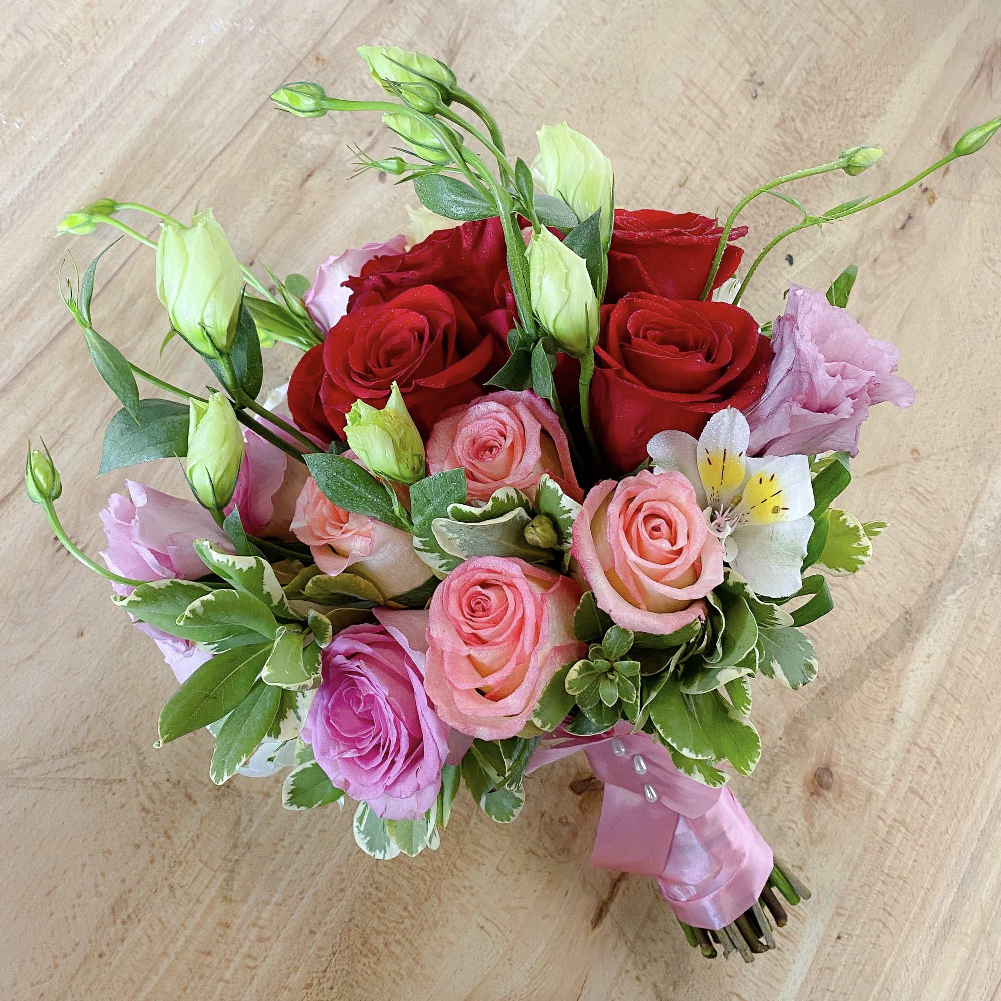 Hand-tied bouquet of red and pink roses with white blooms and ribbon
