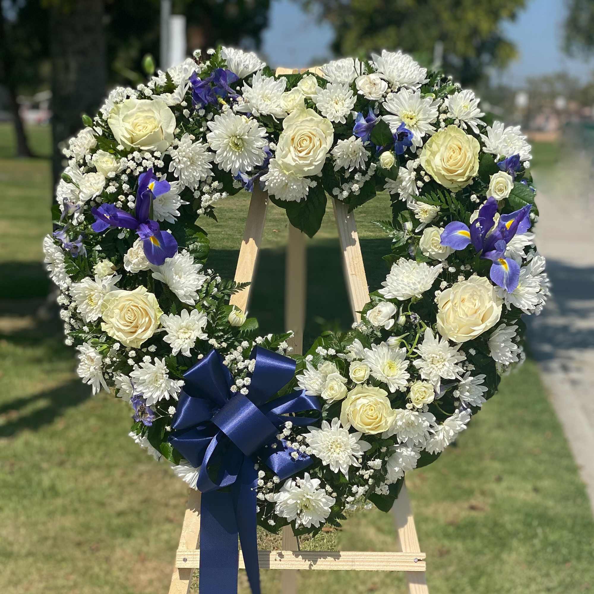 Heart-shaped floral wreath with white roses, daisies, and blue irises on an easel