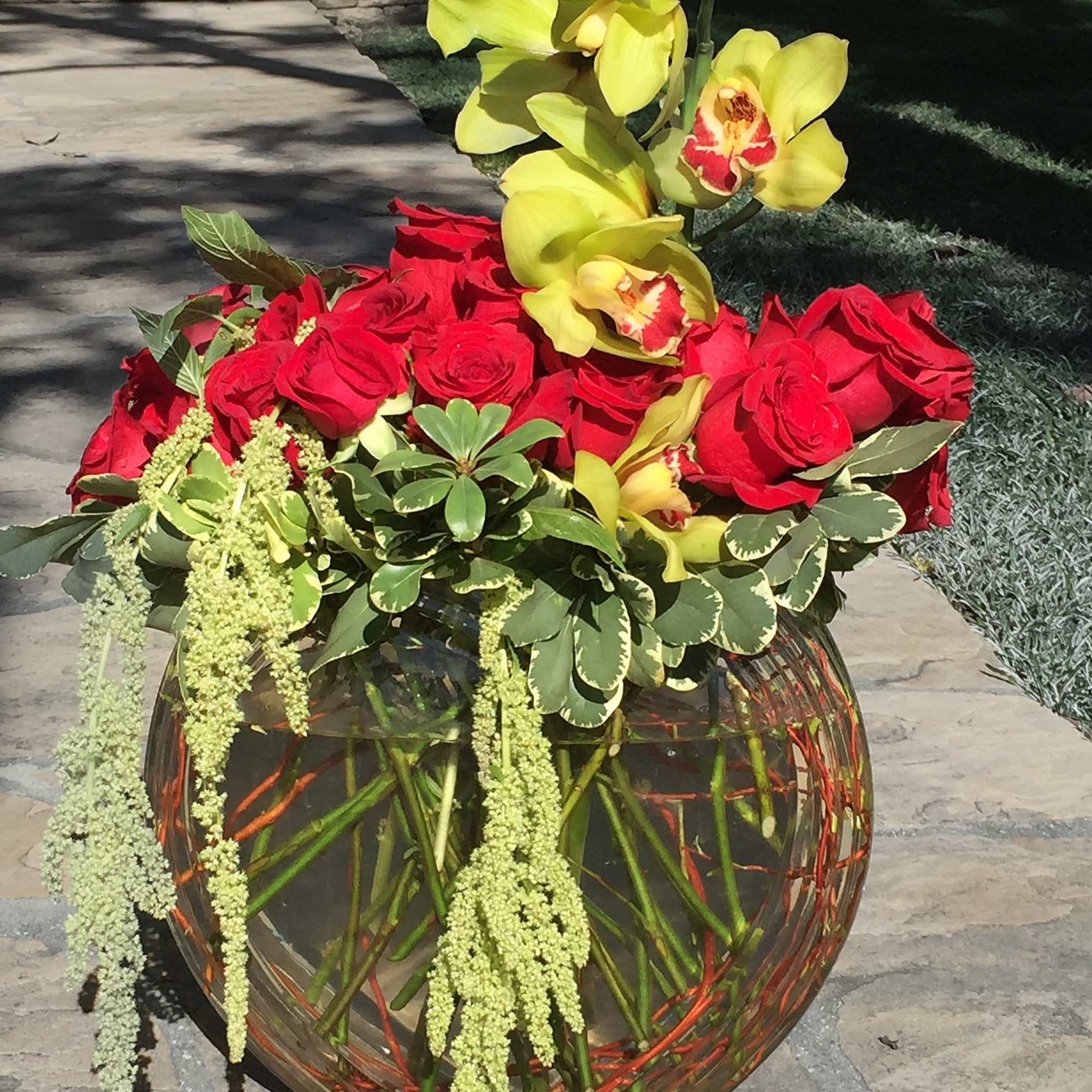 Red roses and yellow orchids in a round glass vase