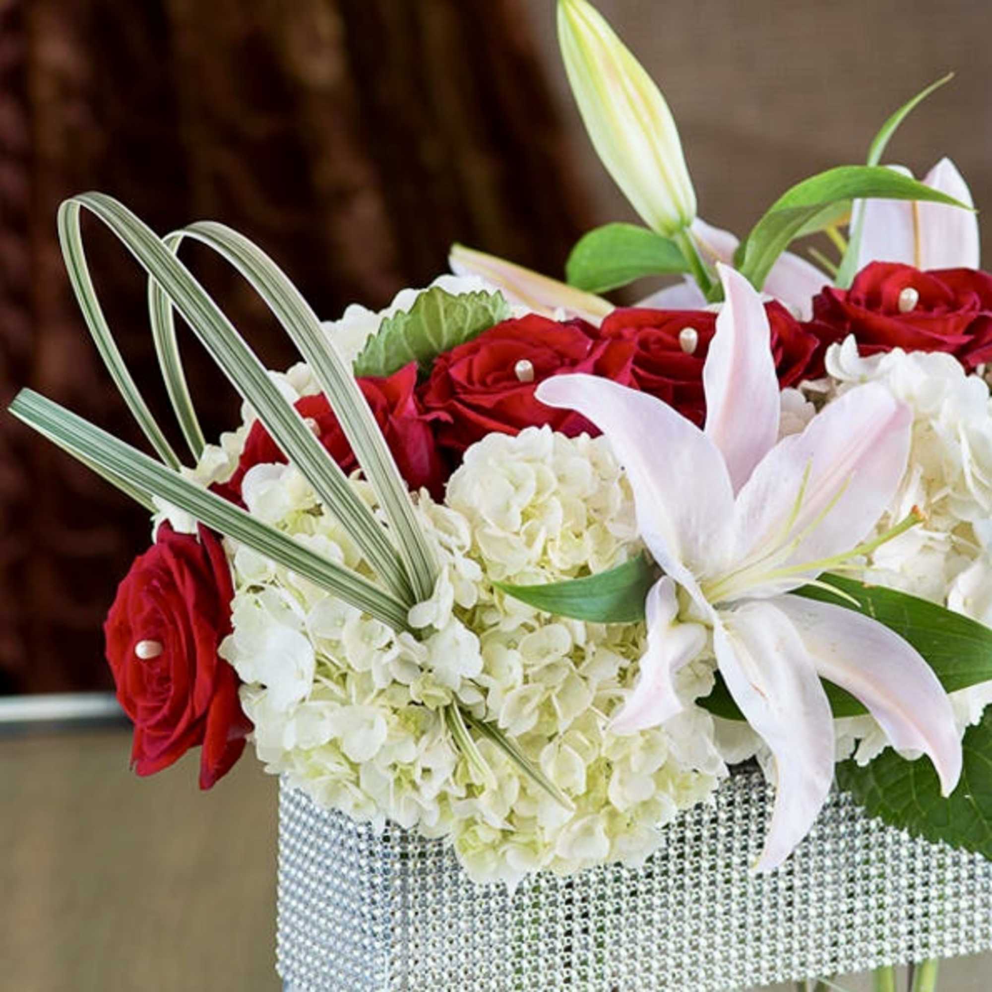 Red roses, white hydrangeas, and pale lilies in a sparkling vase