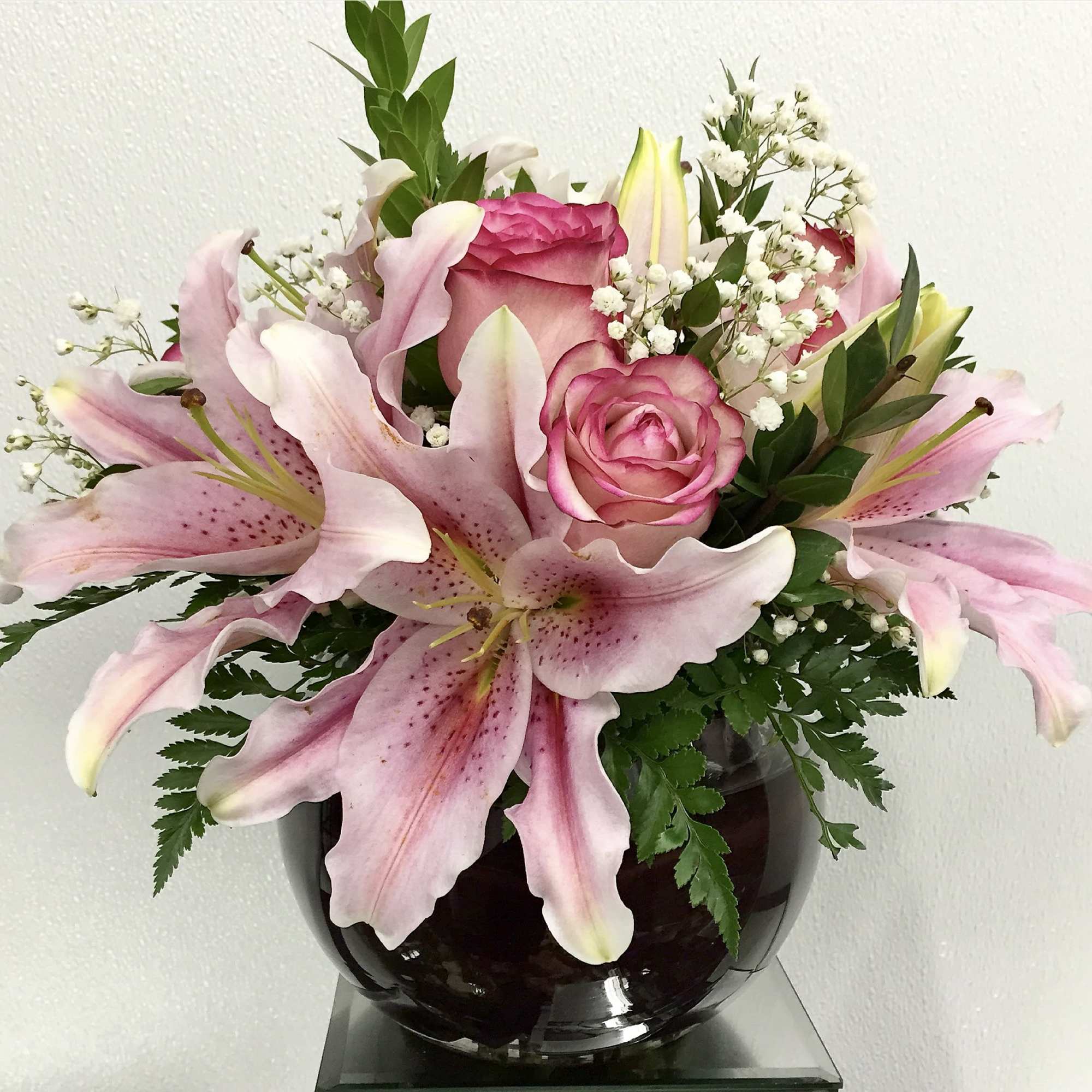 Pink lilies and roses arranged in a dark glass vase
