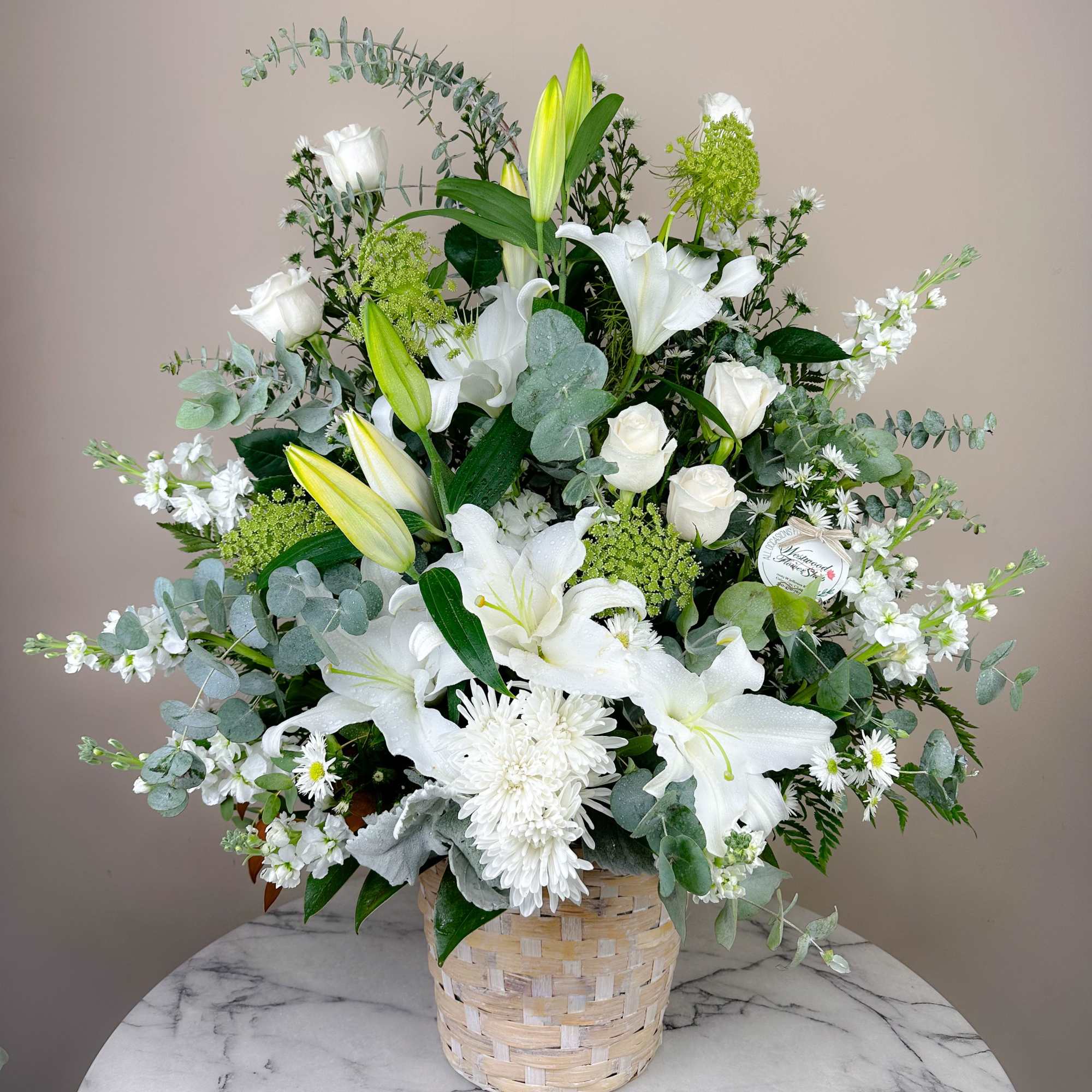 A wispy white and green basket featuring silver dollar eucalyptus and white
