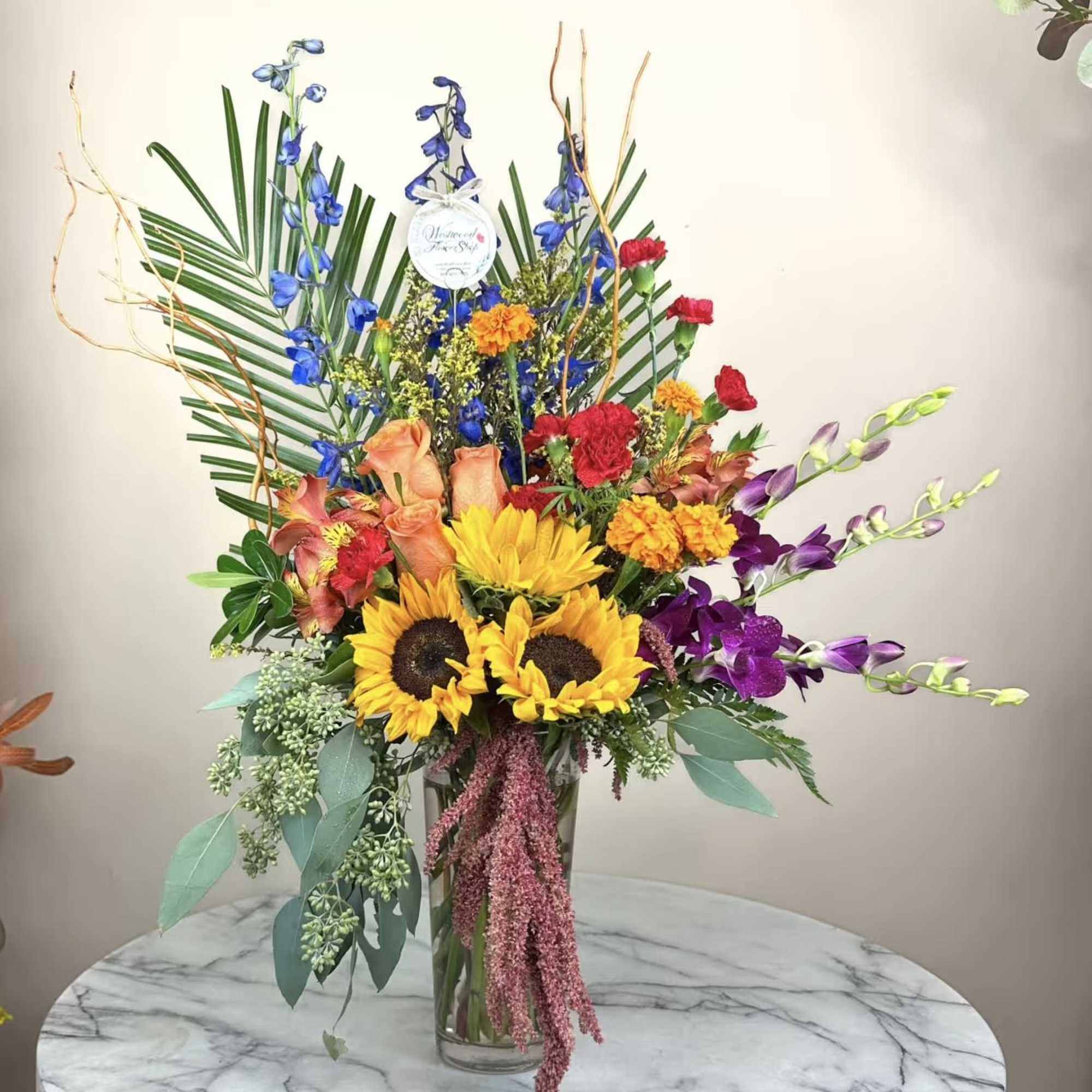 Tall mixed bouquet in a glass vase with sunflowers, orchids, and carnations
