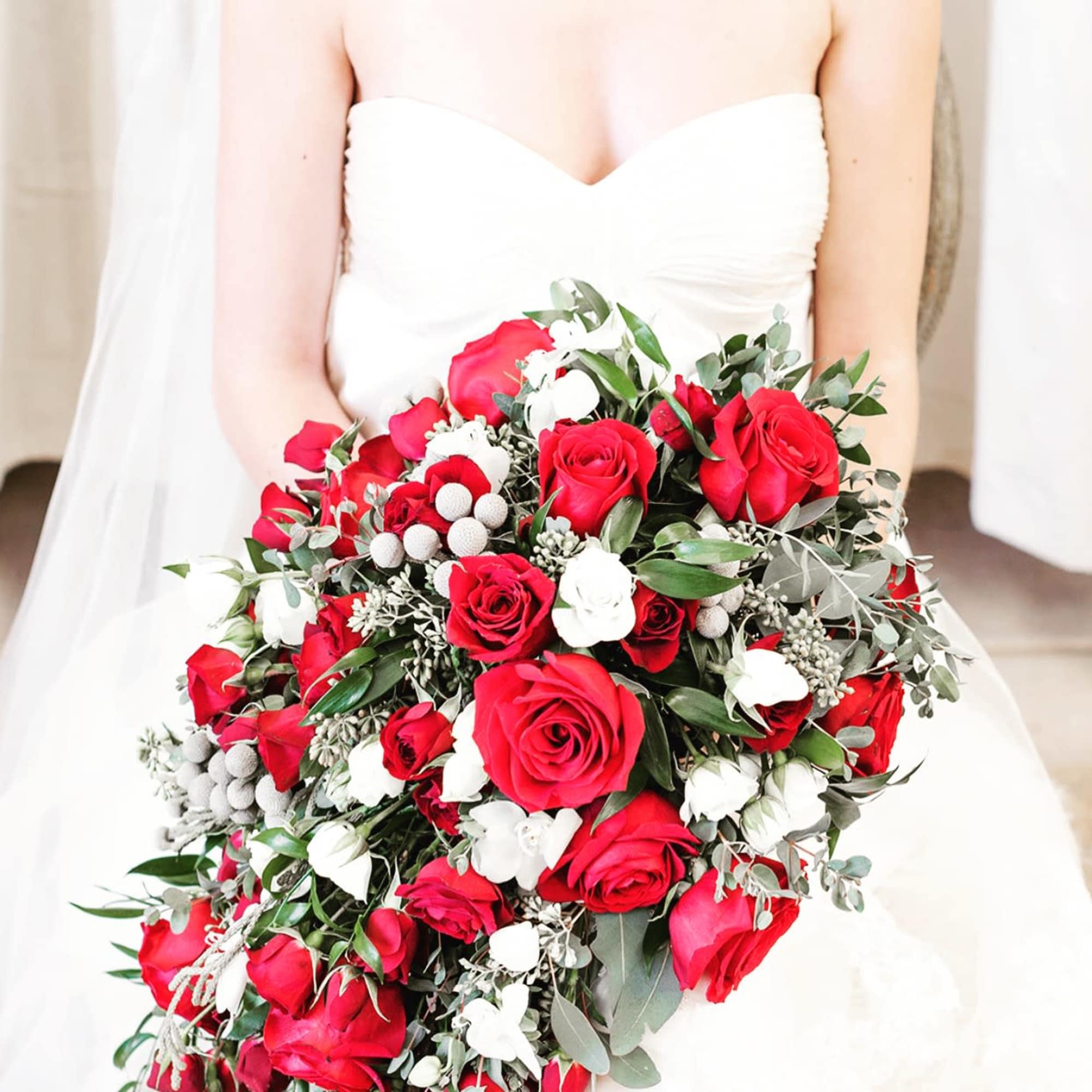 Bride holding a bouquet of red and white roses with greenery