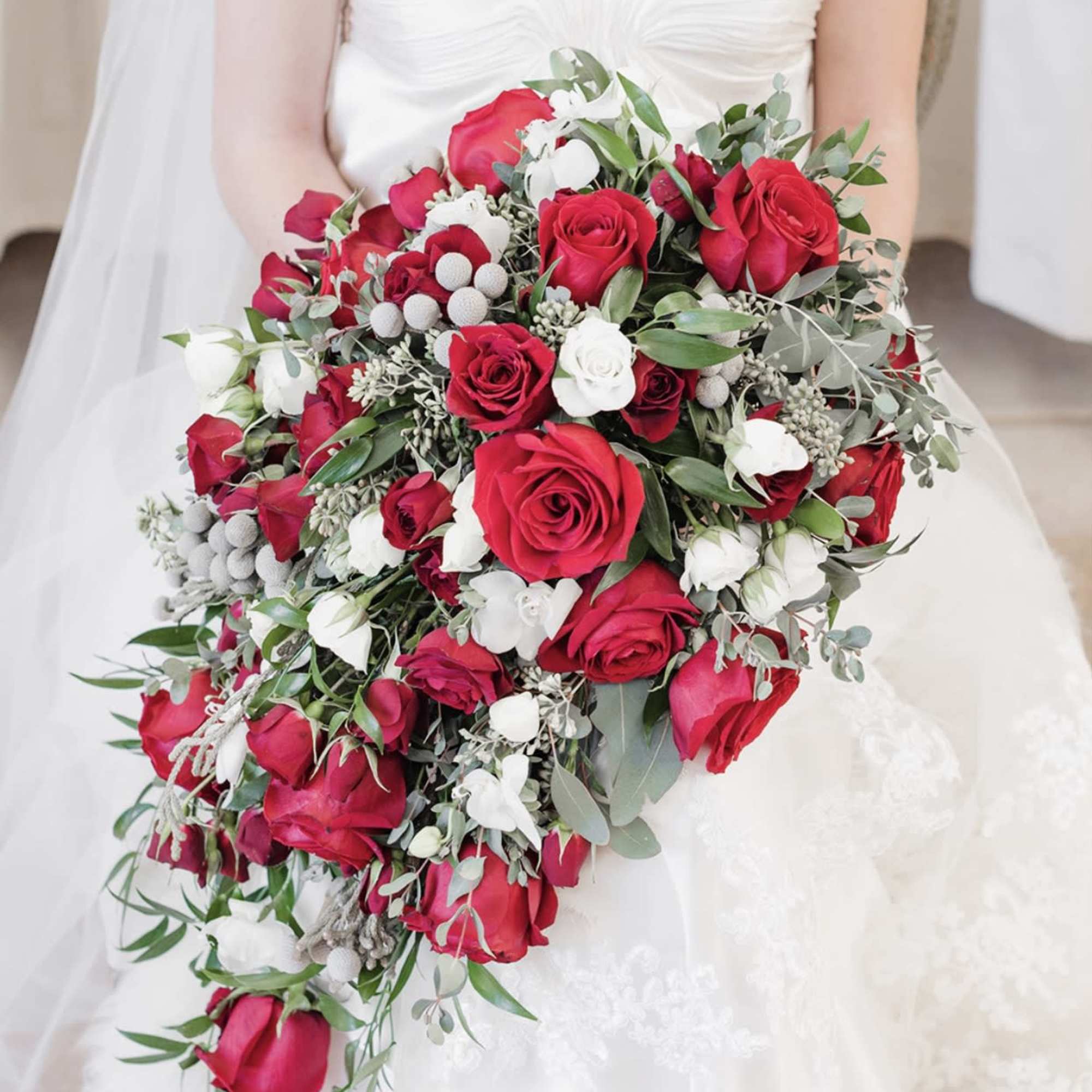 Bride holding a cascading bouquet of red and white roses, photo 3 of 4
