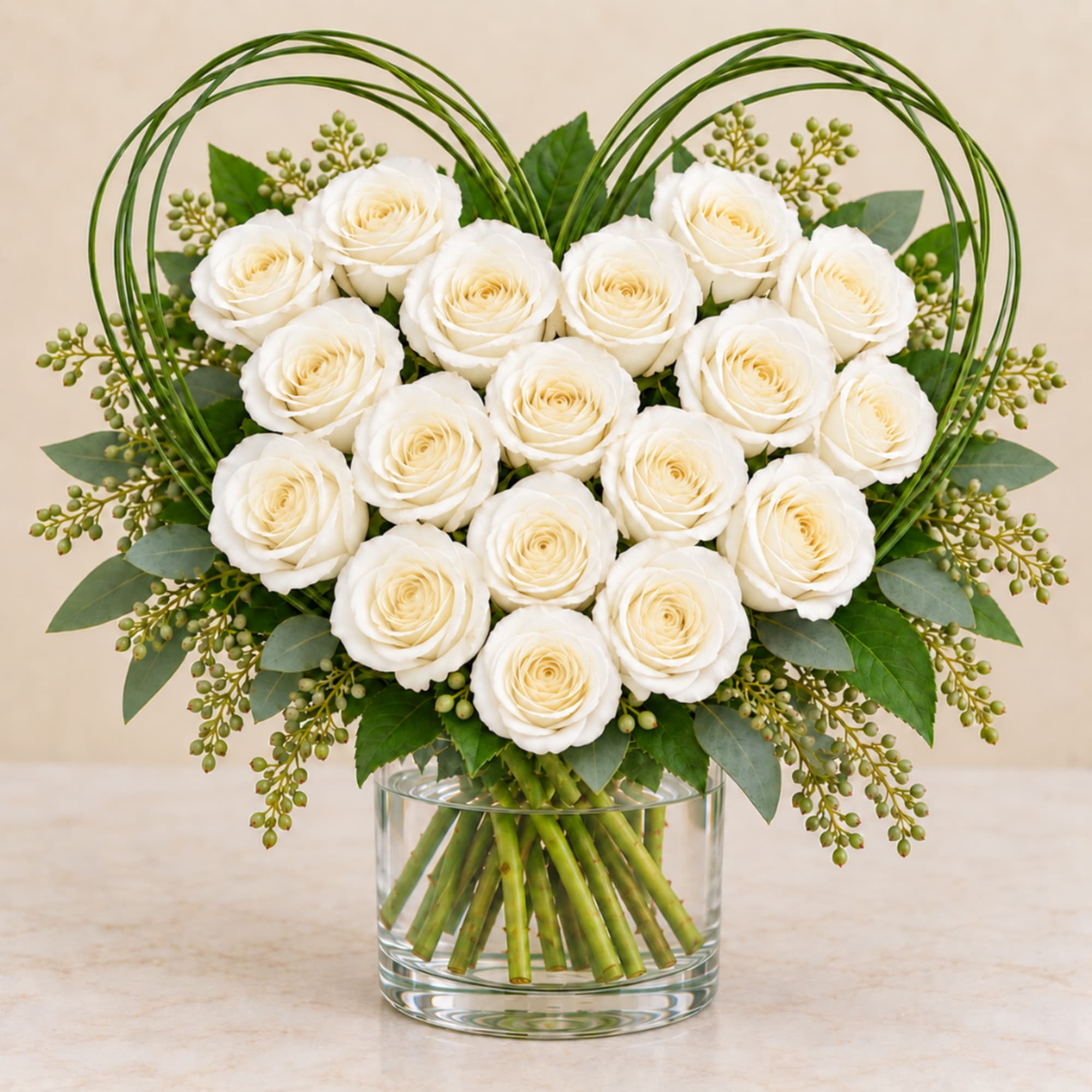 White roses arranged in a clear glass vase with green accents