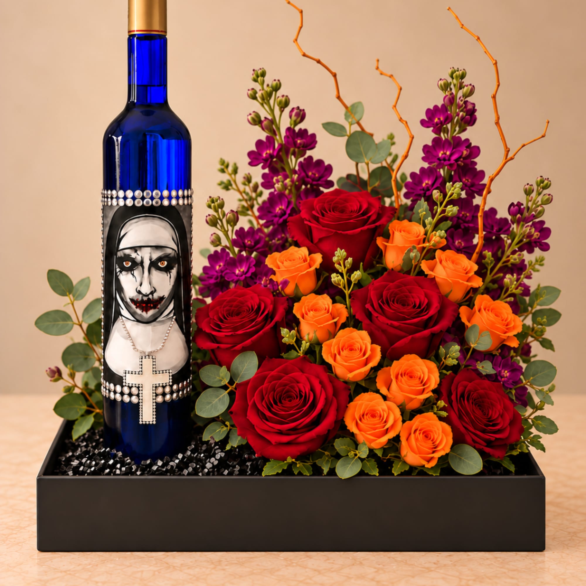 Red and orange roses with purple flowers arranged beside a decorated blue bottle