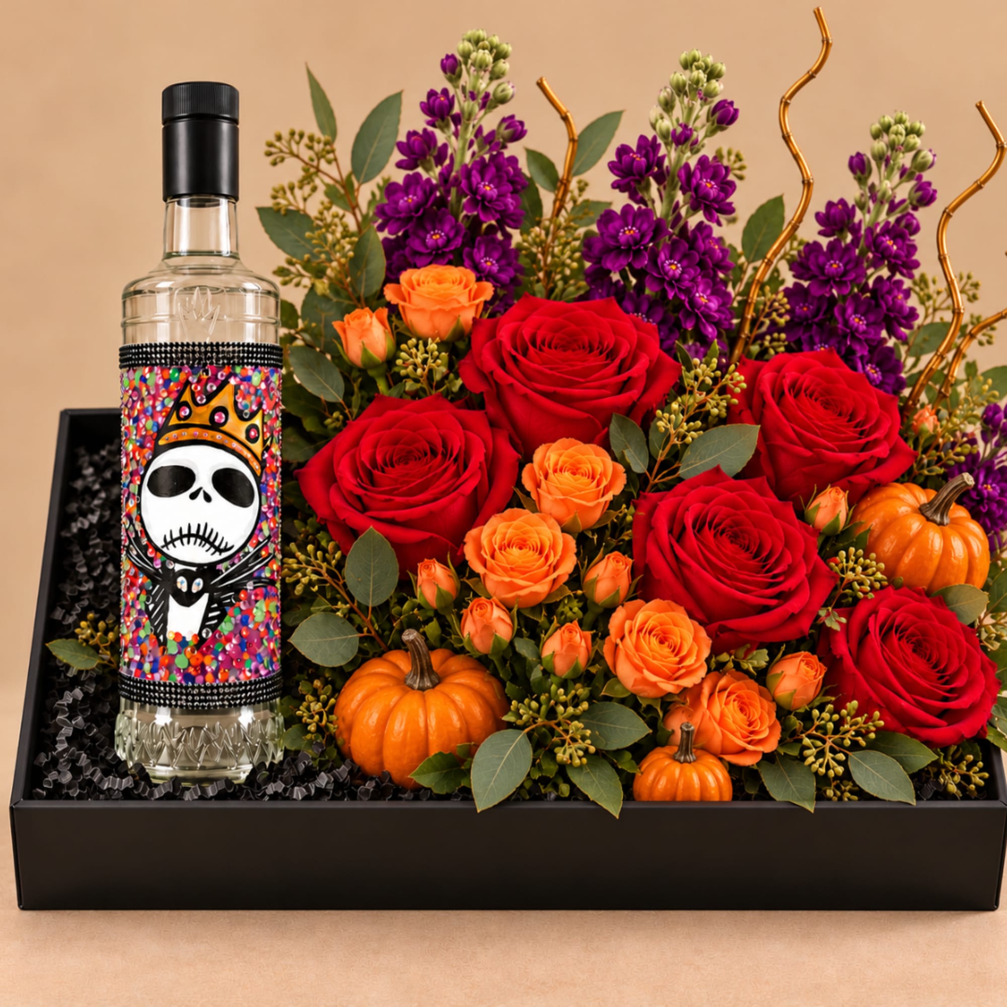 Red and orange roses with purple flowers in a black gift box beside a decorated bottle