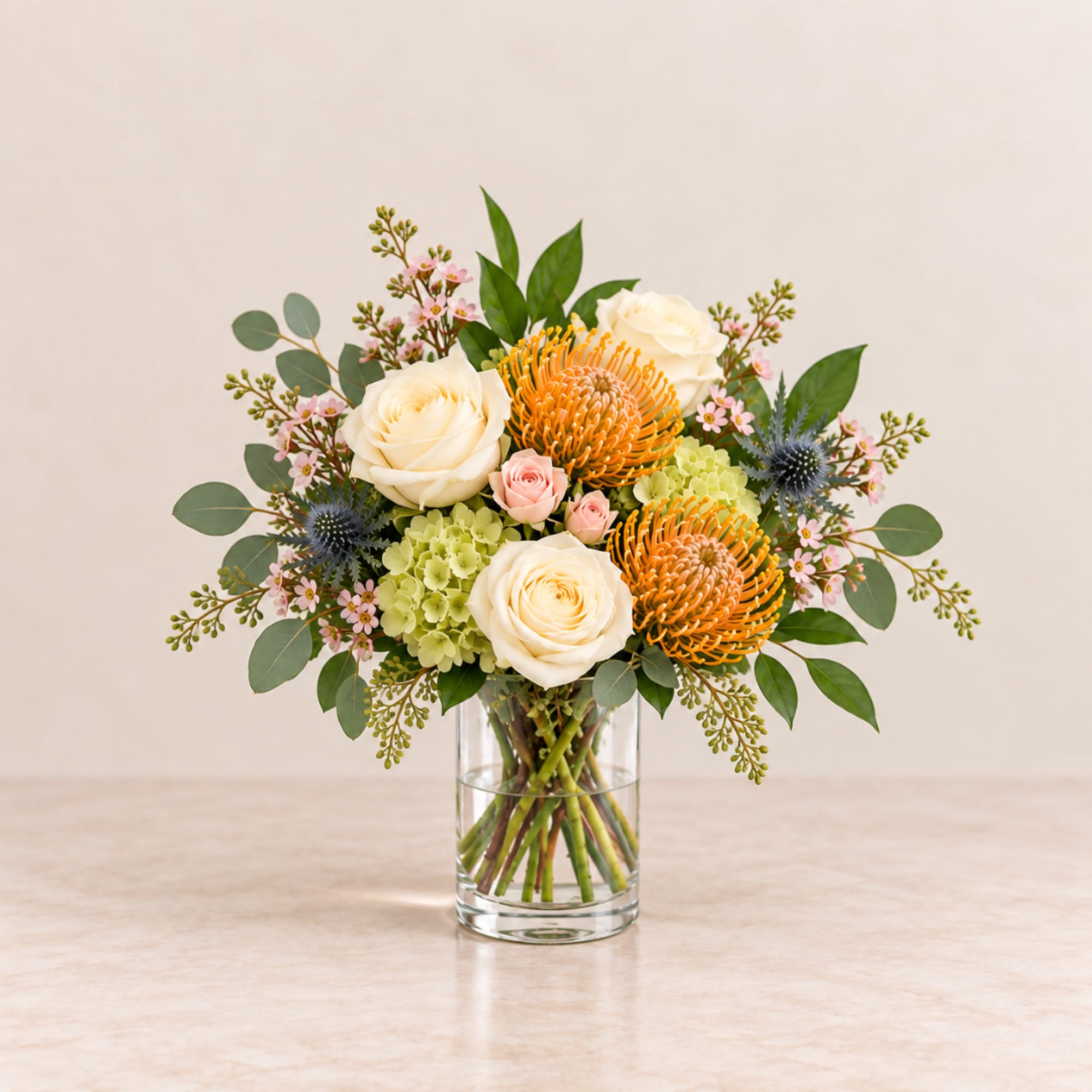 Bouquet of cream roses, orange pincushion blooms, and pink flowers in a glass vase