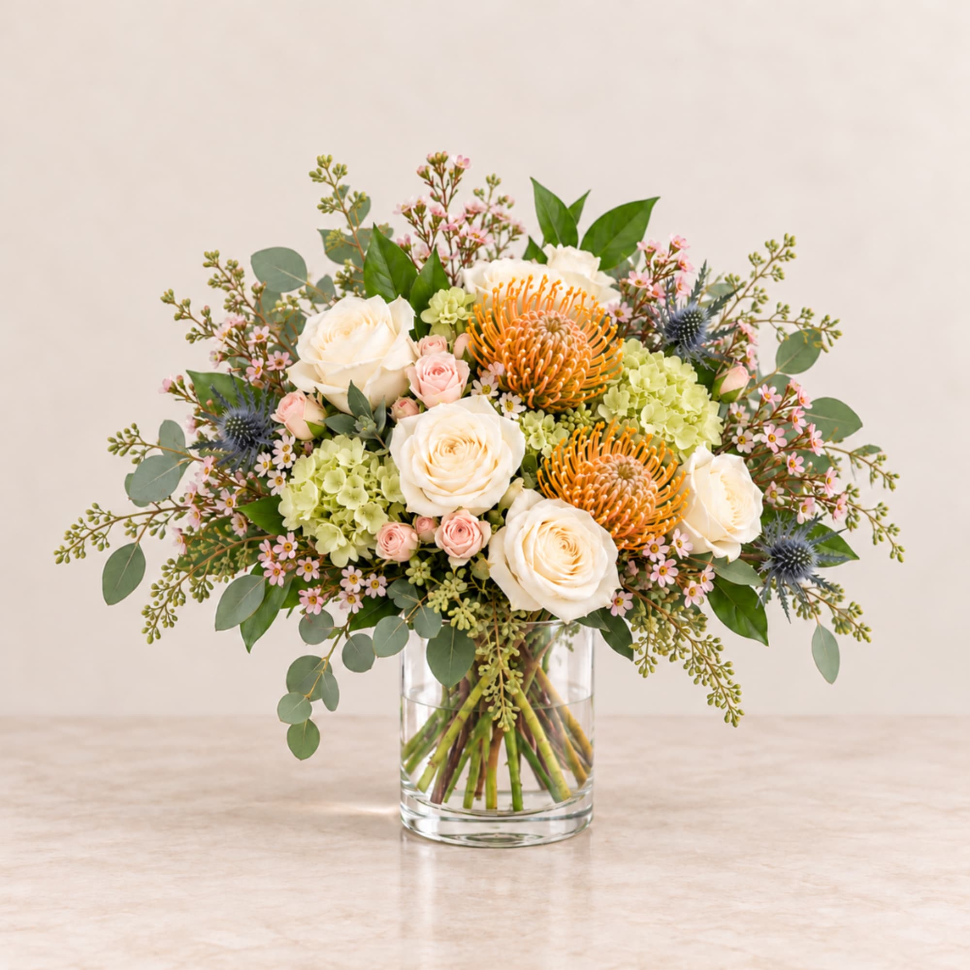Bouquet of cream roses, orange pincushion blooms, and pink accents in a glass vase