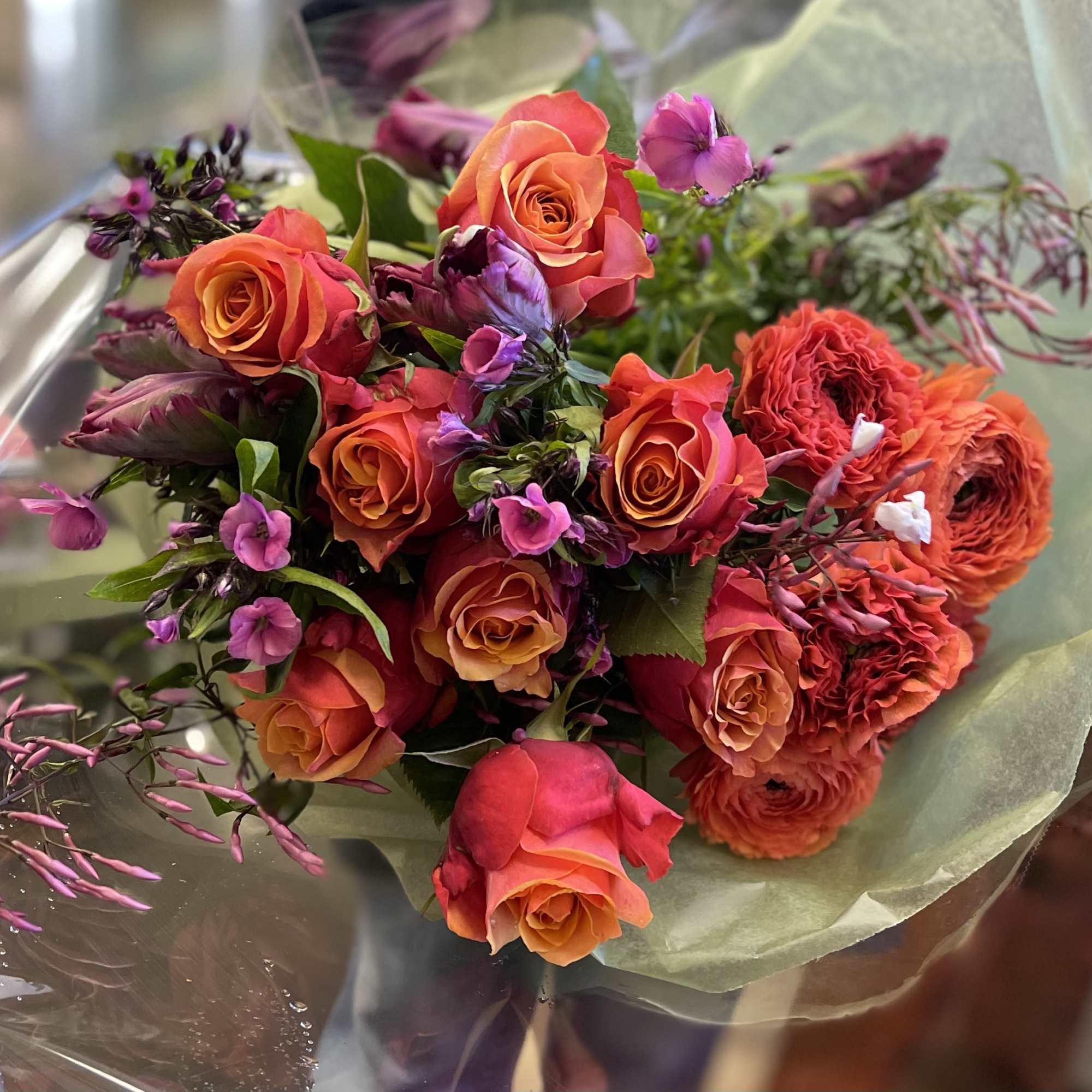 Bouquet of orange roses and purple flowers wrapped in clear paper
