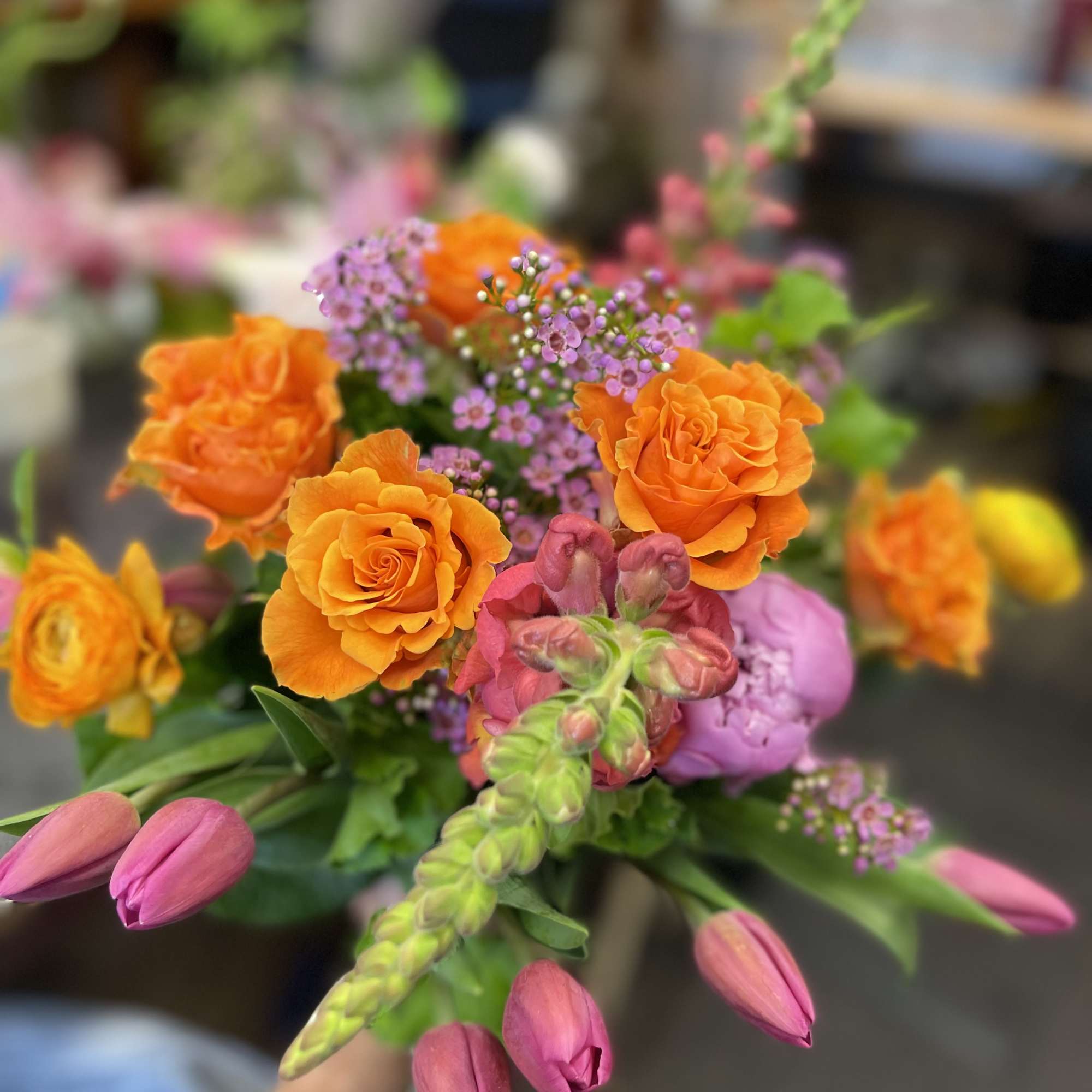 Handheld bouquet of orange roses, pink tulips, and purple filler flowers